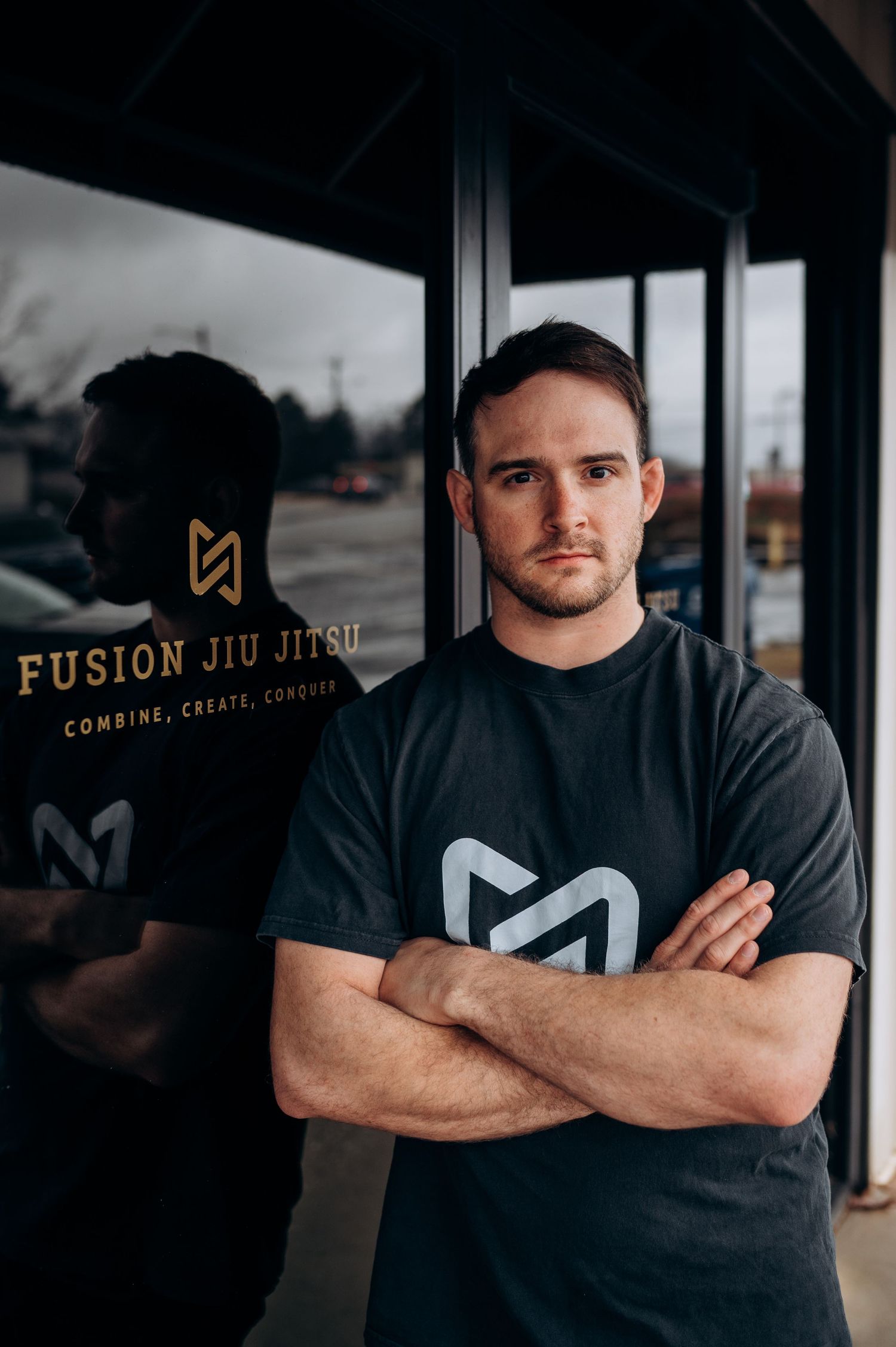 Professional portrait series of a martial arts instructor in front of a modern jiu jitsu studio with dark moody lighting.
