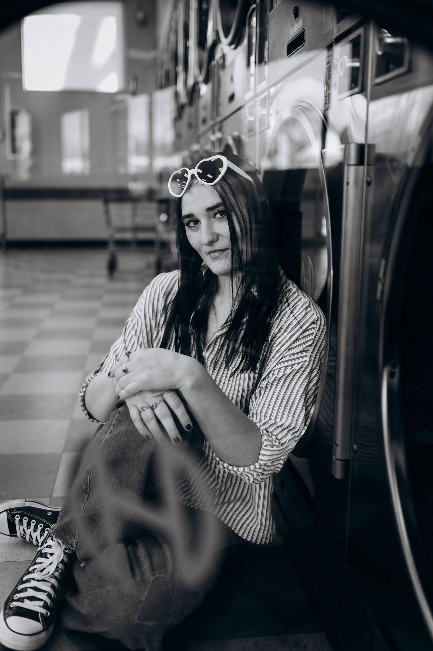 Artistic black and white portrait shot at laundromat with vintage washing machines in background.