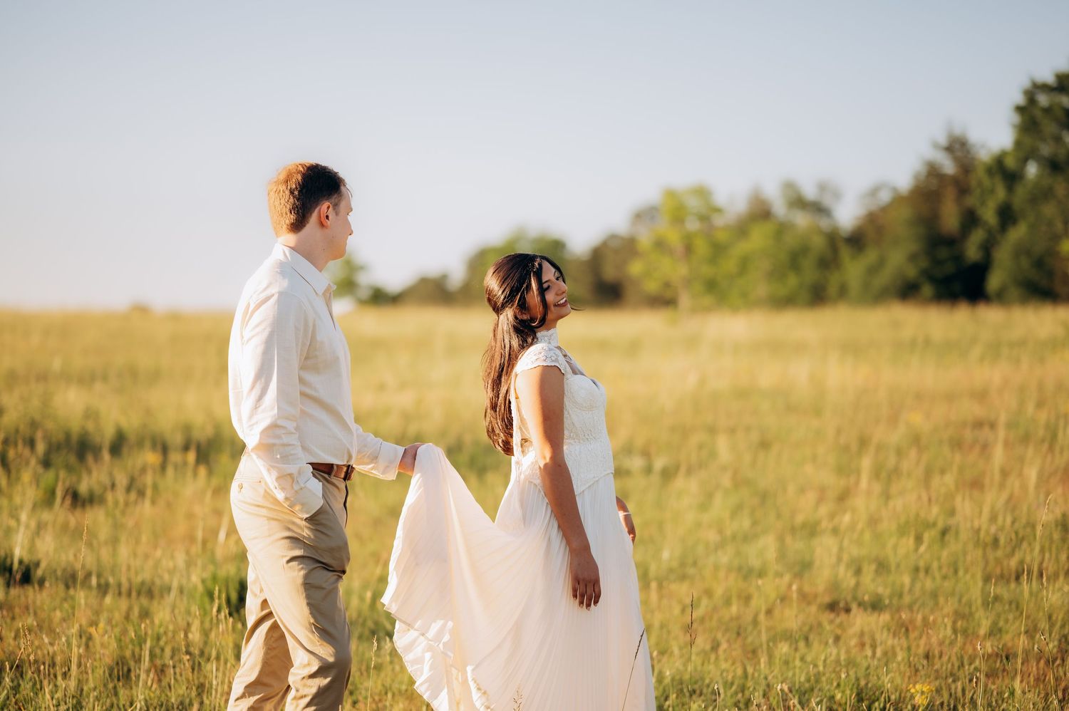 Bride and groom walking hand in hand through a golden sunlit meadow on wedding day.