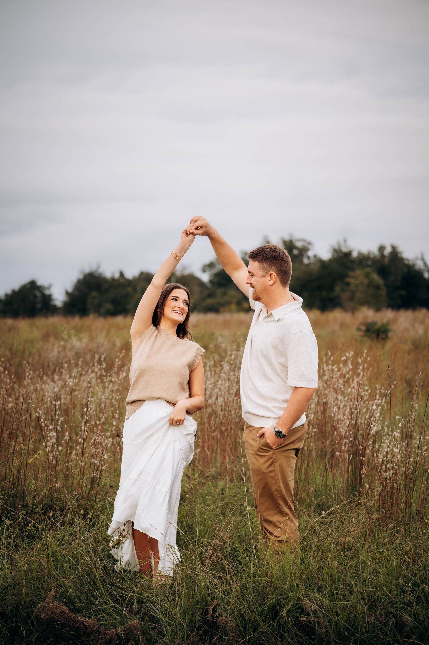 Couple dances and laughs together in a sunlit field with wild grasses.
