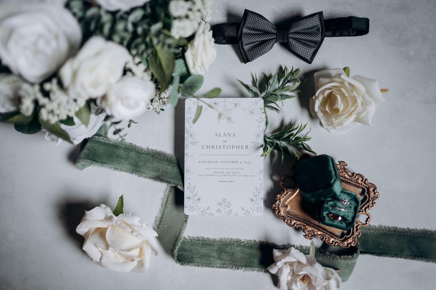 Wedding details including white roses, invitations, and elegant accessories arranged on a light gray surface.