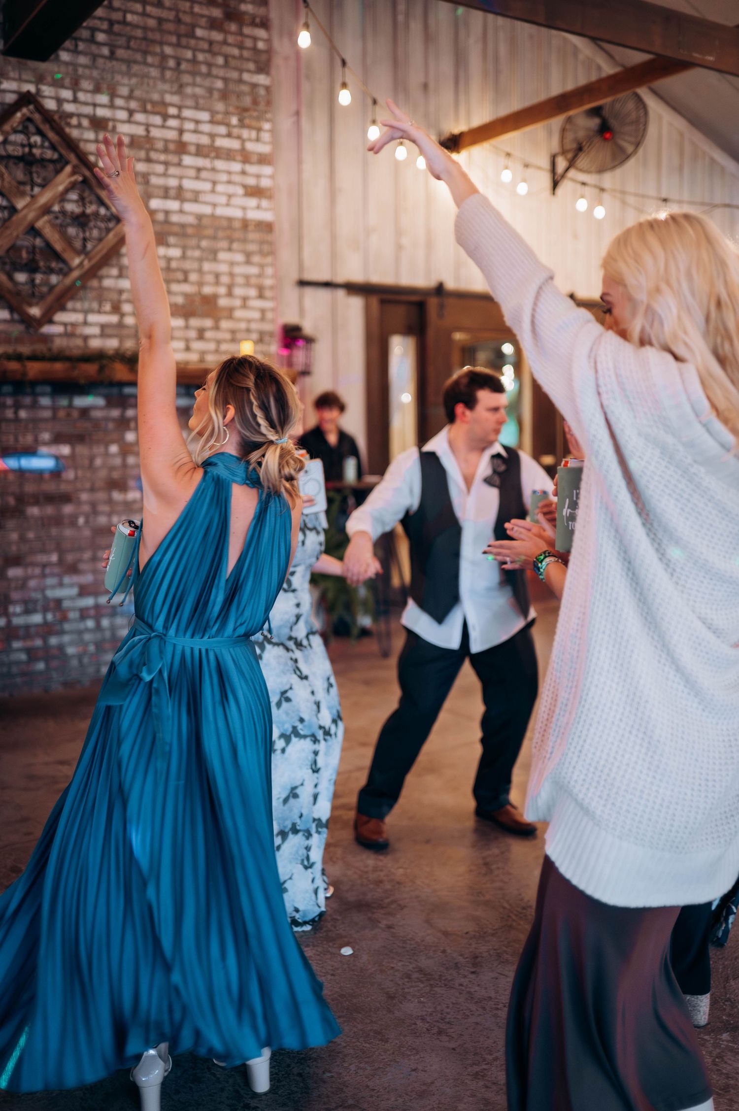Guests dancing energetically in a rustic venue decorated with string lights and exposed brick walls.