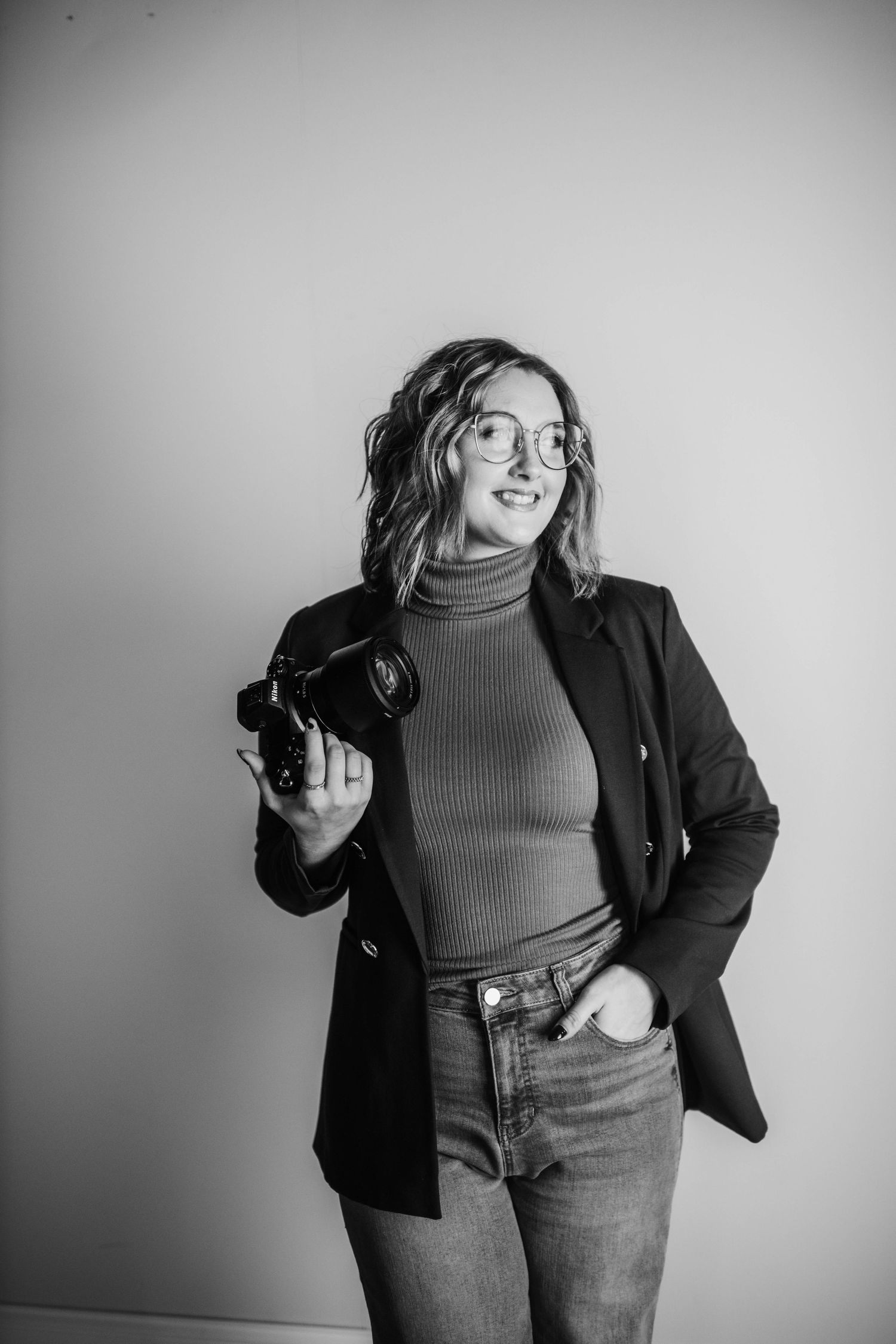Black and white studio portrait of photographer with camera gear in professional attire.