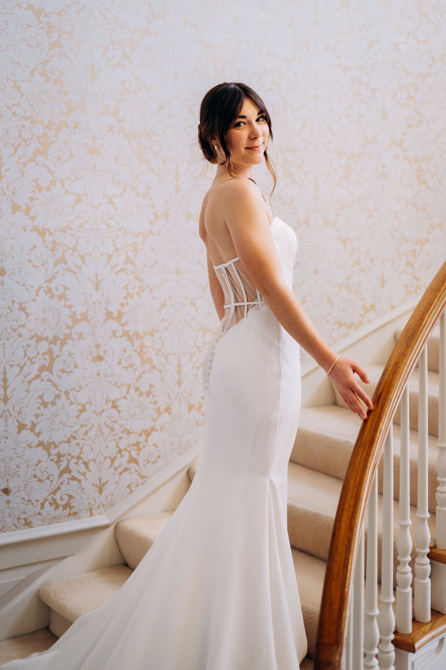 Bride in a fitted white gown with corset back posing elegantly on a grand staircase.