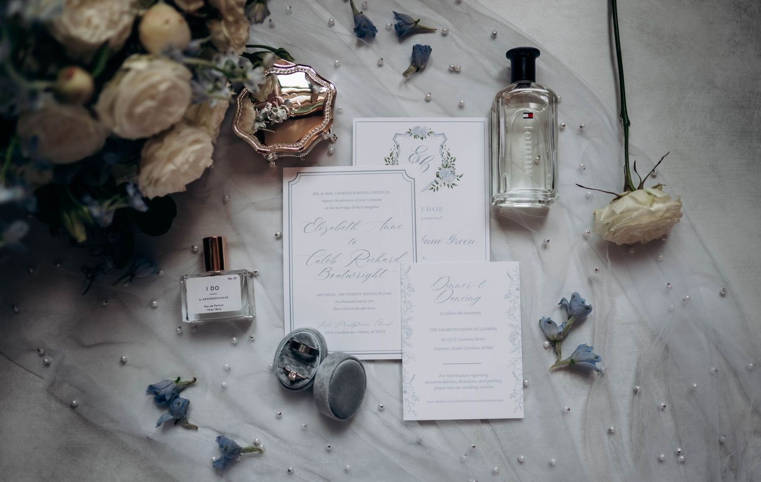 Wedding details including perfume bottles, invitations, and delicate floral arrangements on a light surface.