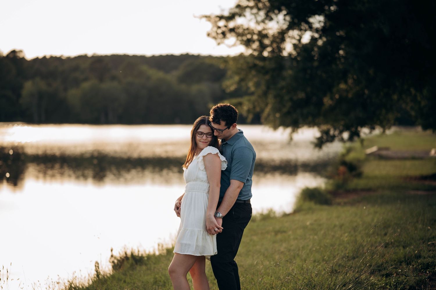 Silhouettes of a couple embrace near a tranquil lake during golden hour photography session.