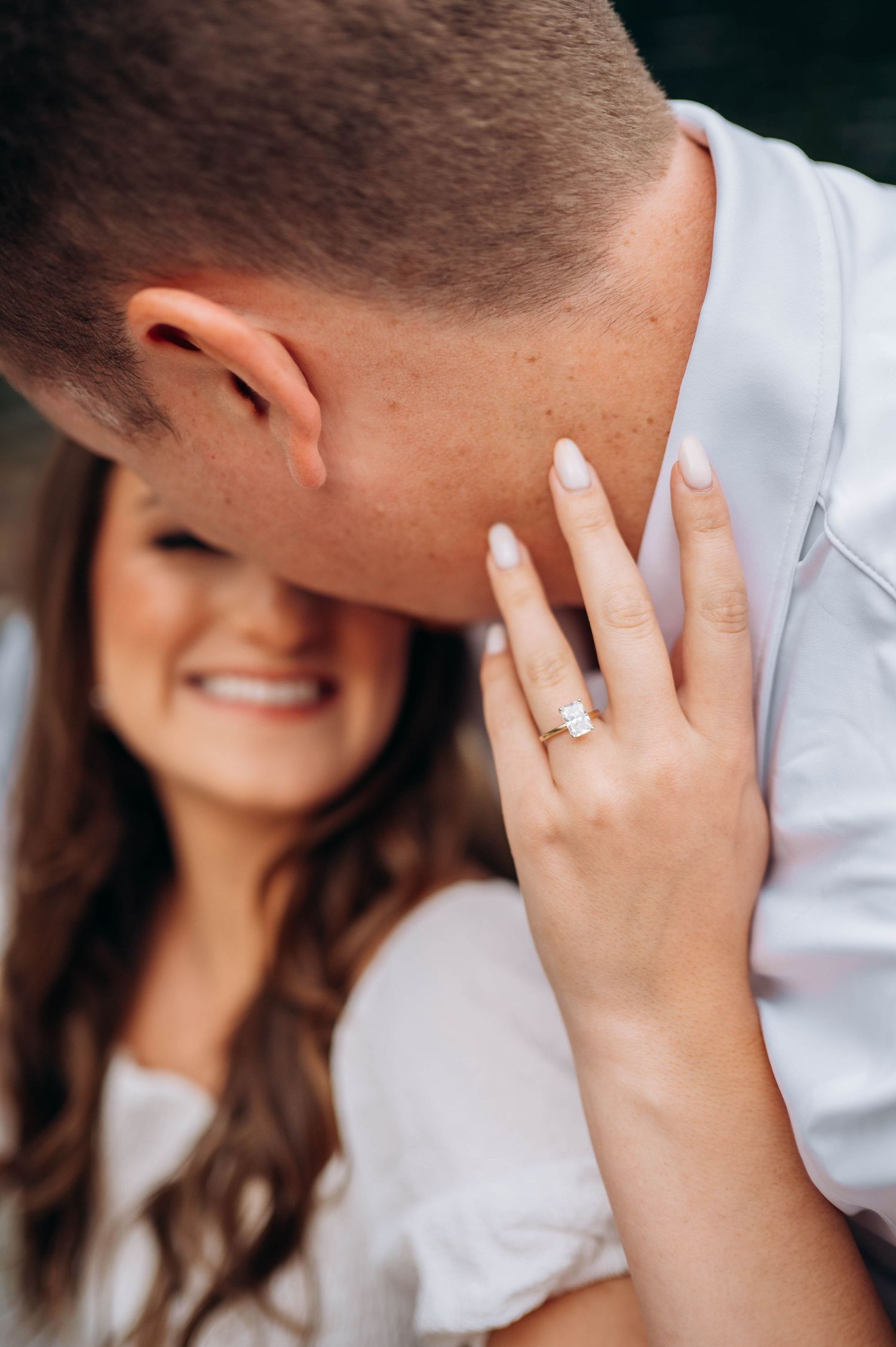 Close-up of an engagement ring as a couple shares an intimate moment by the water.
