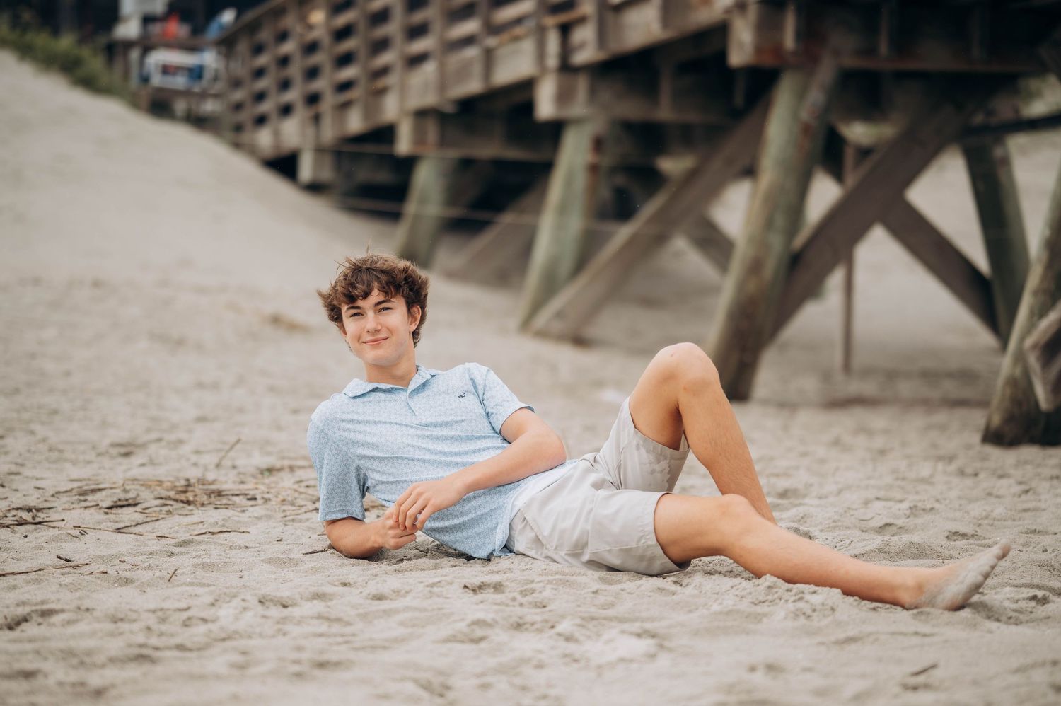 Person lounging on sandy beach beneath a wooden pier structure.
