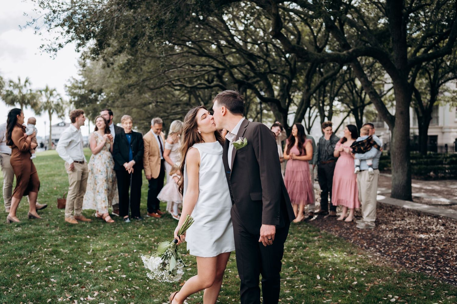 Wedding party poses for photos in an outdoor garden setting with pink and white attire.