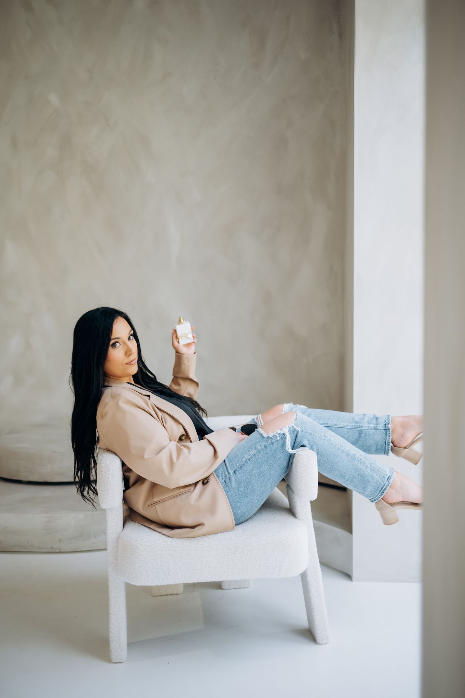 Woman relaxes on white bench while using smartphone in minimalist setting.