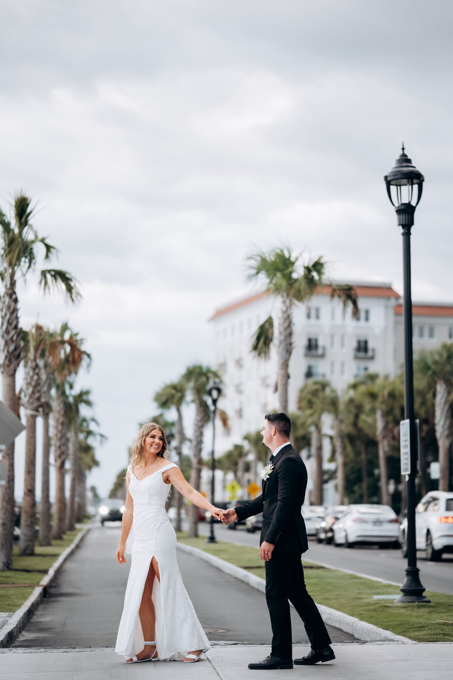 Bride and groom holding hands on palm tree-lined boulevard on their wedding day.