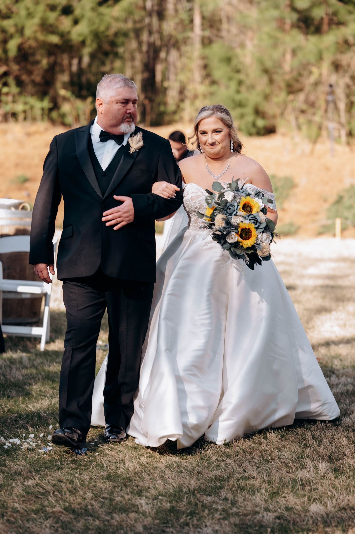 Elegant outdoor wedding scene with white dress and sunflower bouquet against autumn backdrop.