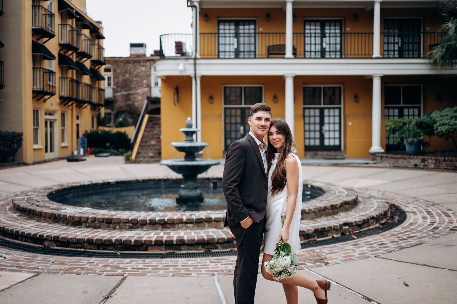 Bride and groom posing elegantly in front of a courtyard fountain at their wedding venue.