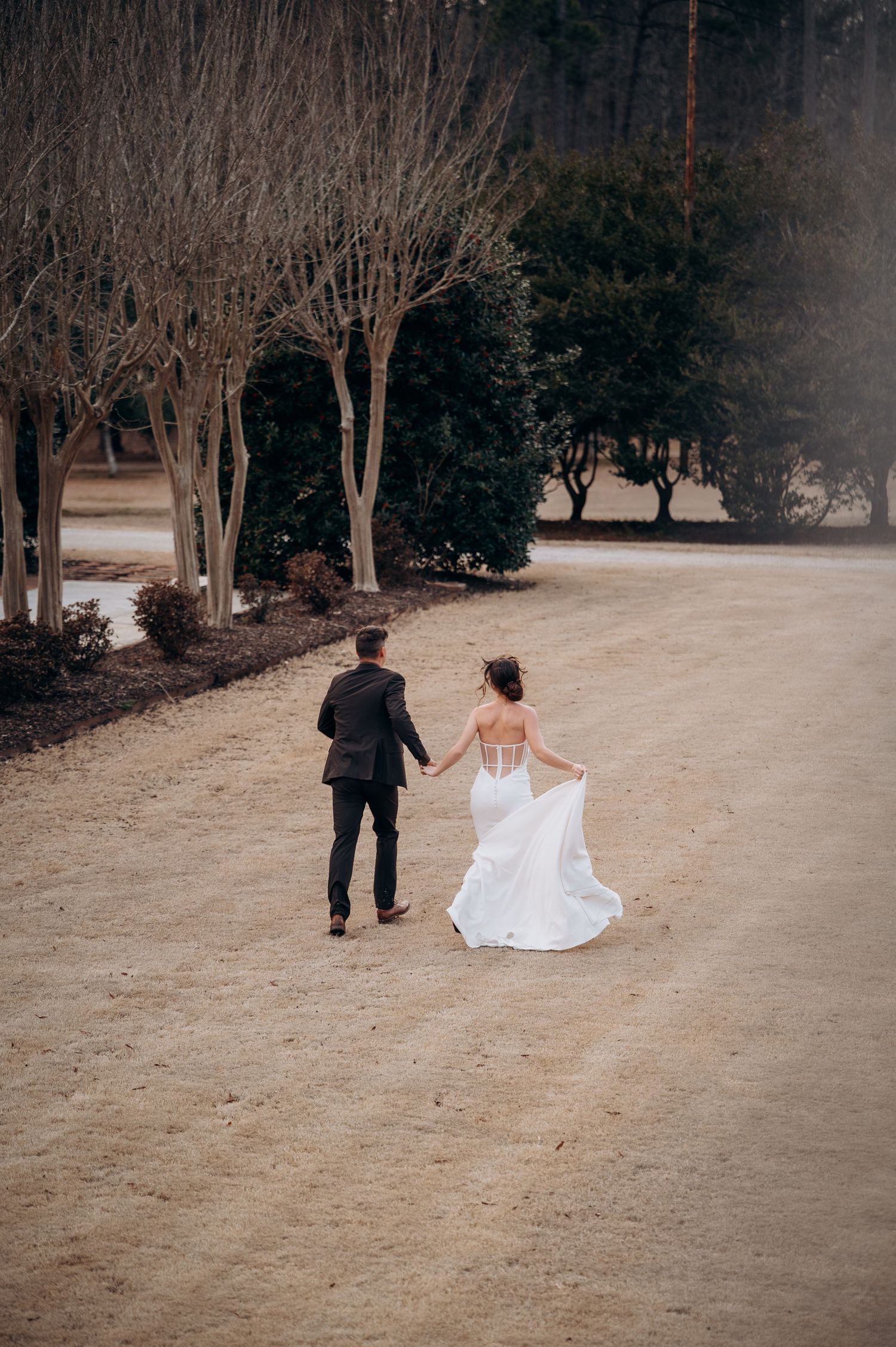 Wedding couple strolls down a scenic gravel path as bride's white gown train flows behind her.