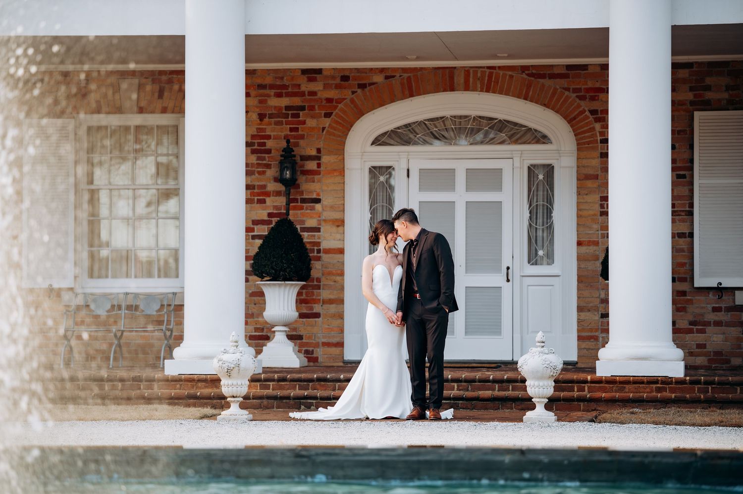 Bride and groom share romantic moment by pool at elegant brick mansion wedding venue.