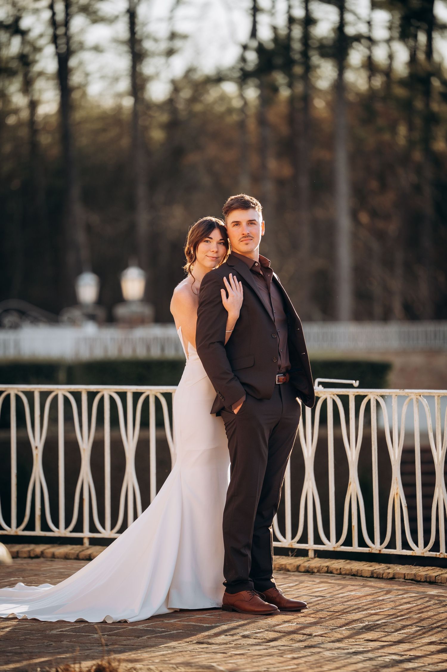 Newlyweds share an intimate moment on a decorative white railing deck during golden hour.
