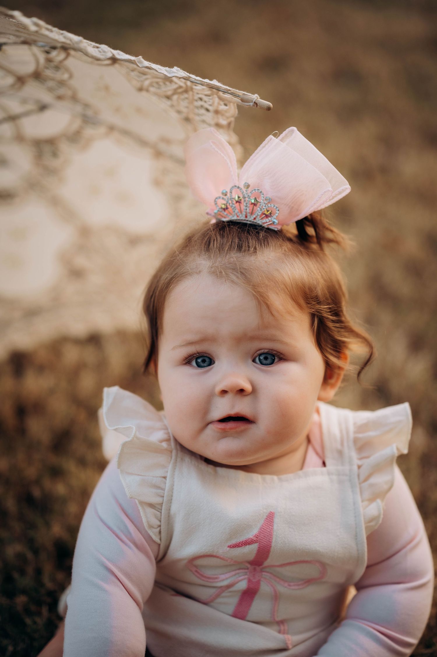 A baby wearing a crown and pink outfit smiles at the camera.