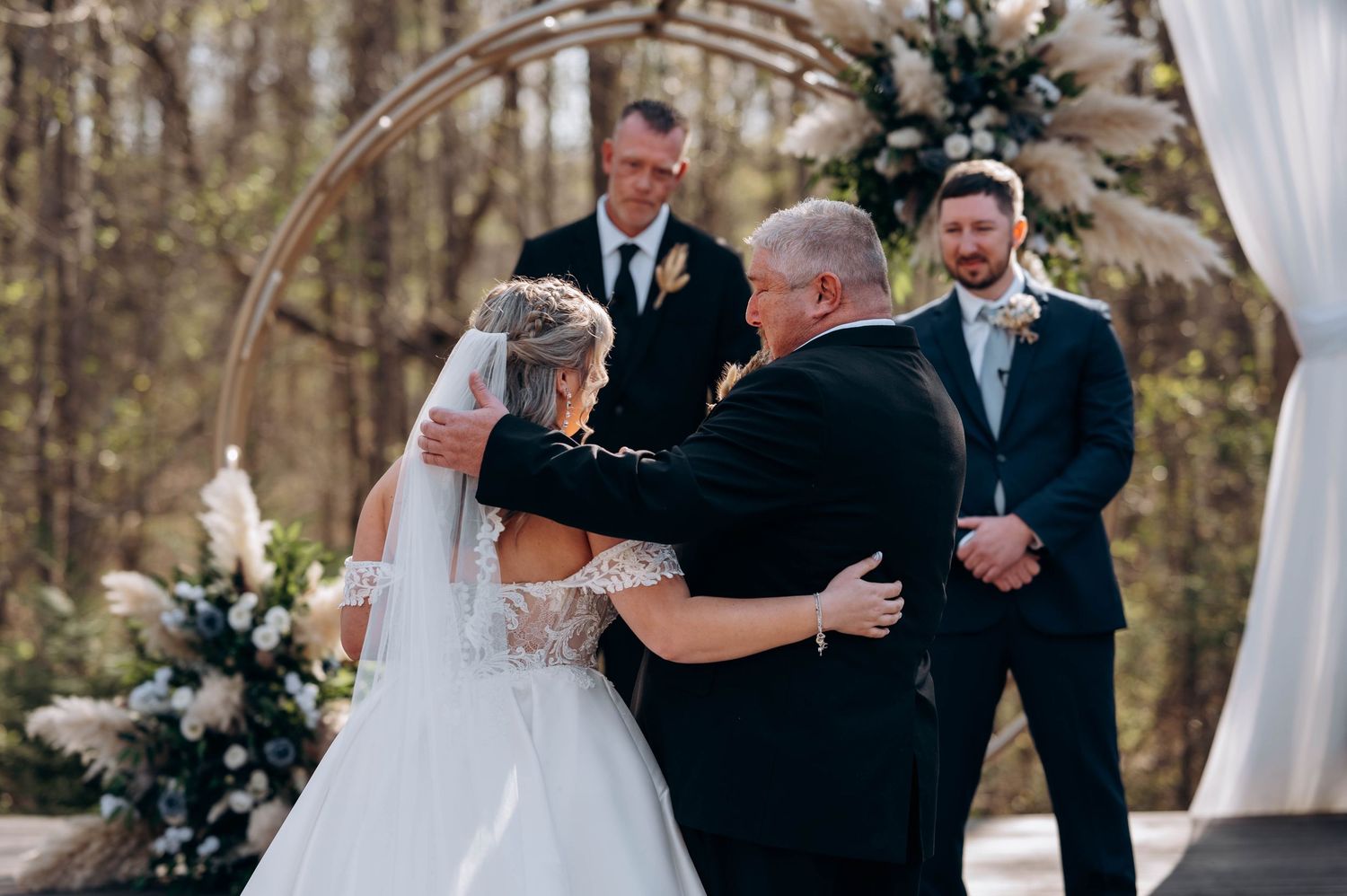 Intimate wedding ceremony moment under decorated arch with white drapery and florals.