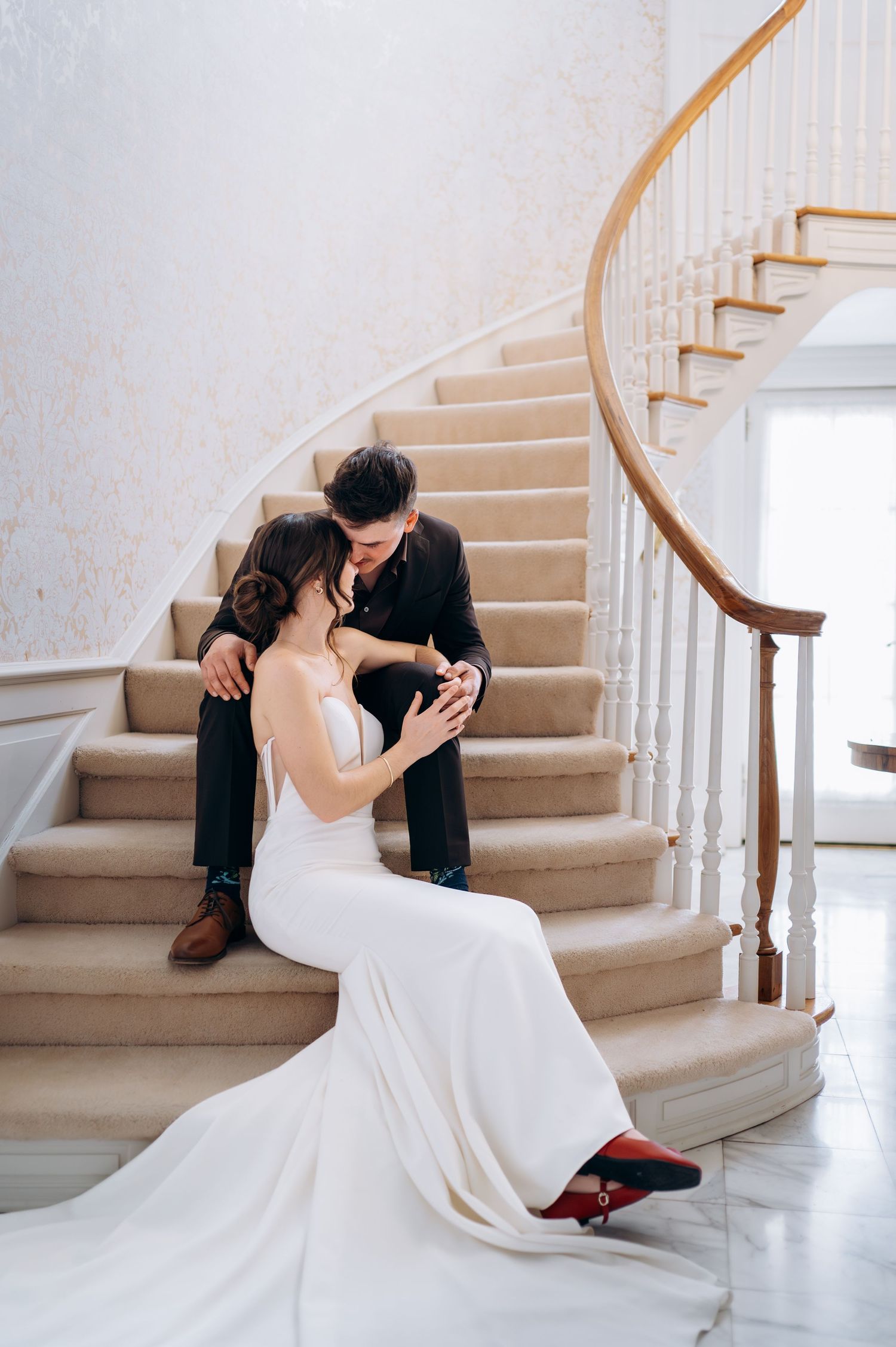 Bride and groom sharing romantic kiss while seated together on grand curved staircase steps.