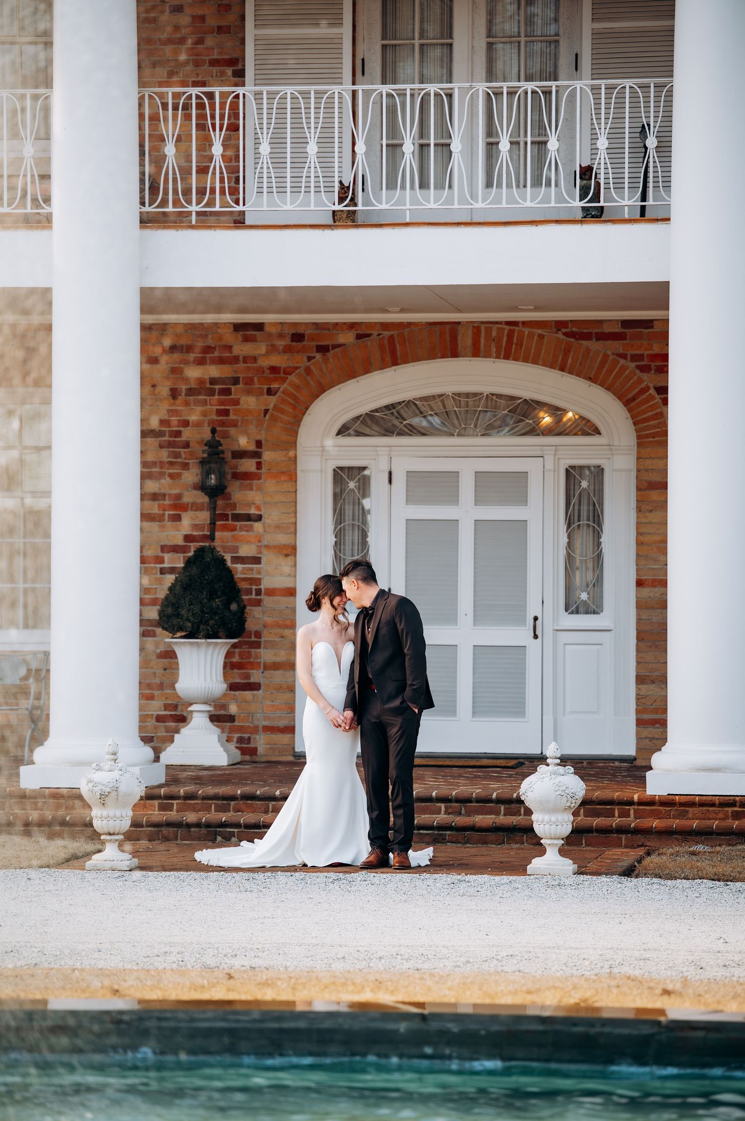 Bride and groom sharing a romantic kiss outside a grand brick estate with columns.