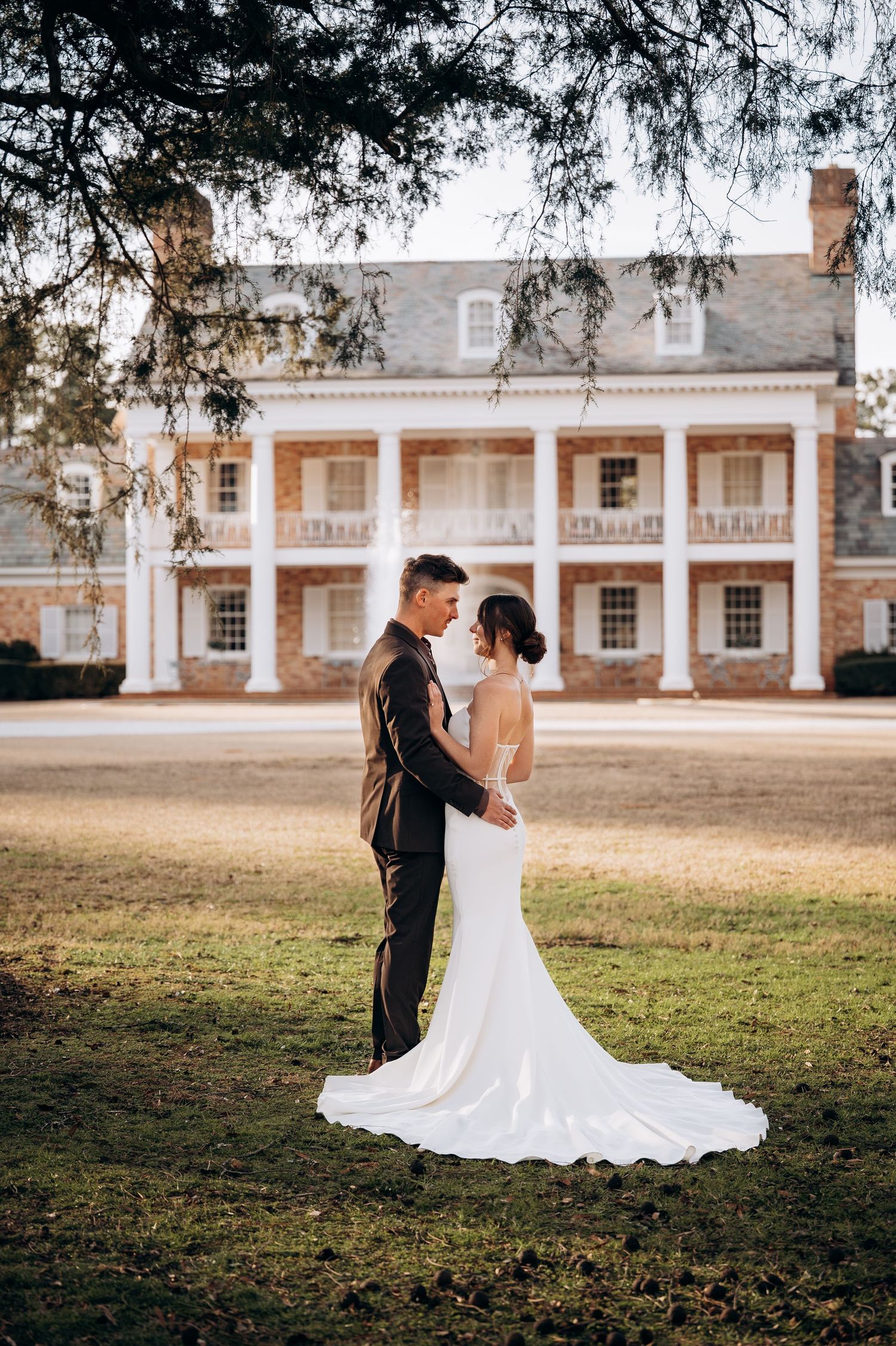 Newlyweds pose together on lawn in front of historic colonial style mansion with white columns.