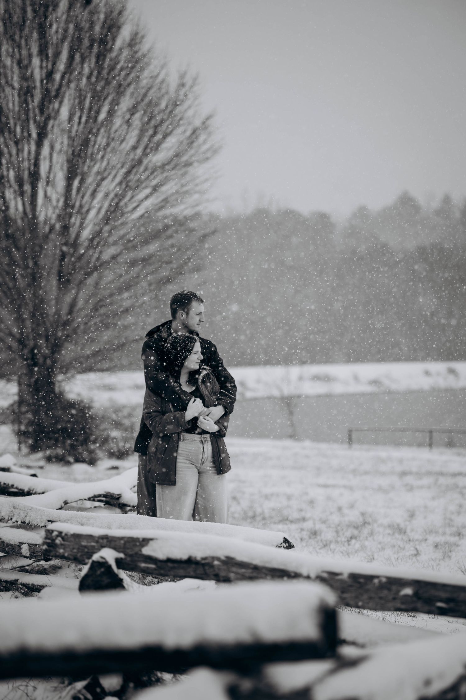 Two figures embrace in a snowy winter landscape during a romantic photoshoot session.