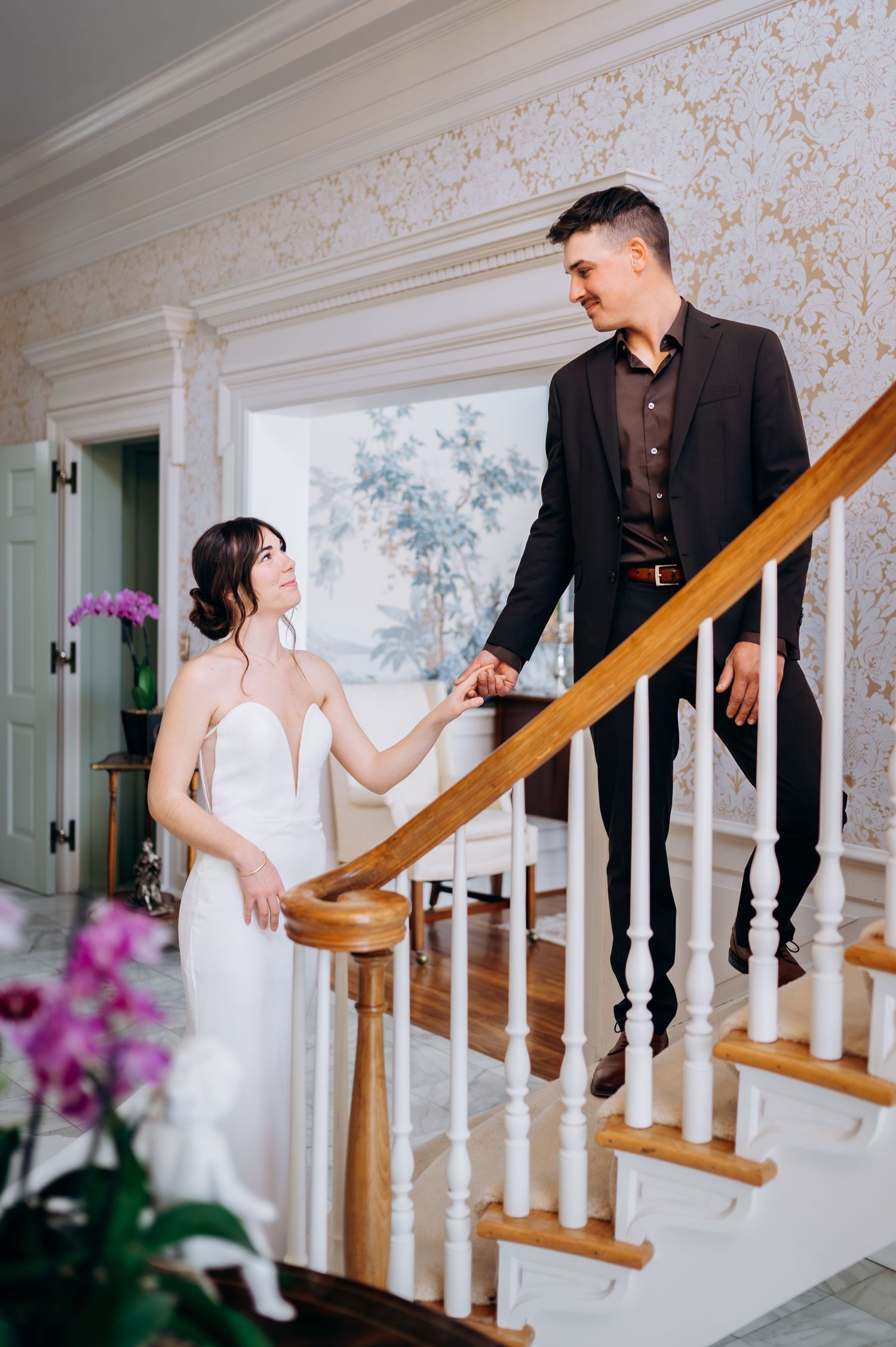 Romantic staircase scene with couple in wedding attire interacting on elegant white stairs.