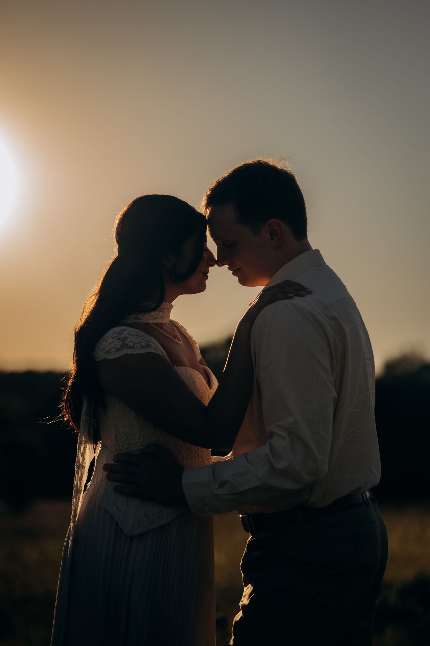 Romantic couple embracing at golden sunset in a field, sharing an intimate moment in wedding attire.
