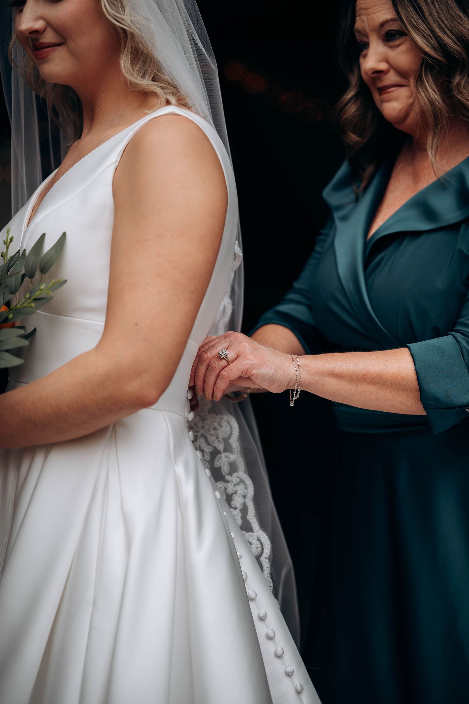 Detail shot of wedding dress being adjusted with lace and buttons visible.