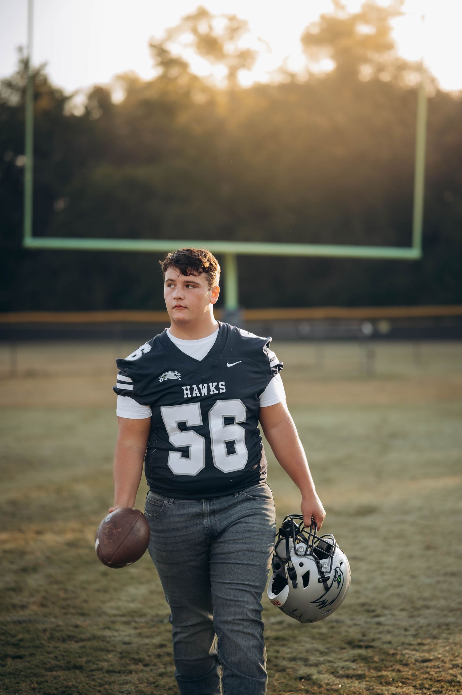 Football player in Hawks jersey number 56 poses on field at sunset with helmet and ball.