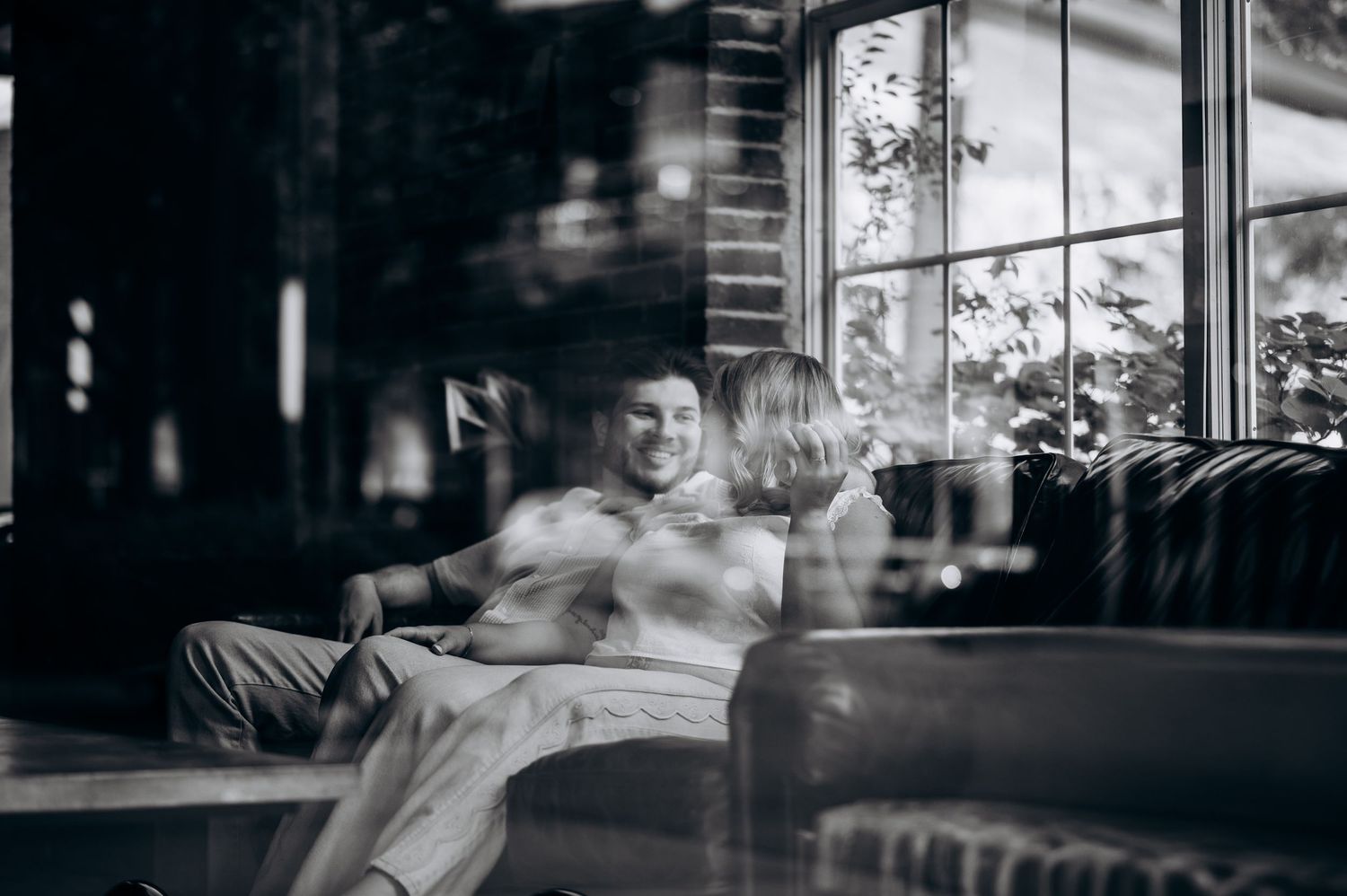 Black and white photo of a smiling couple relaxing together on a couch in a stylish indoor setting.