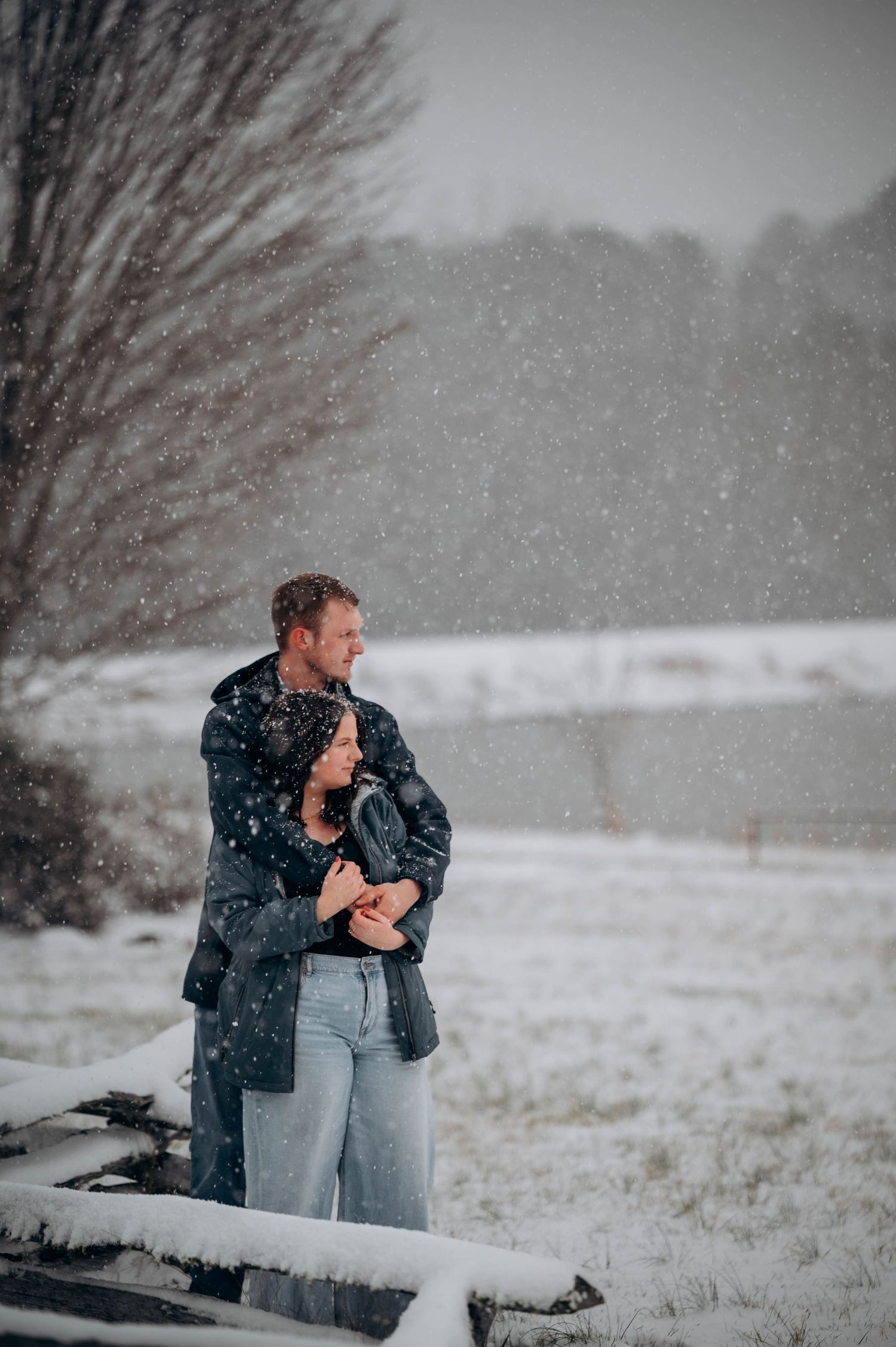 A couple embraces in a snowy winter landscape during a romantic photoshoot.