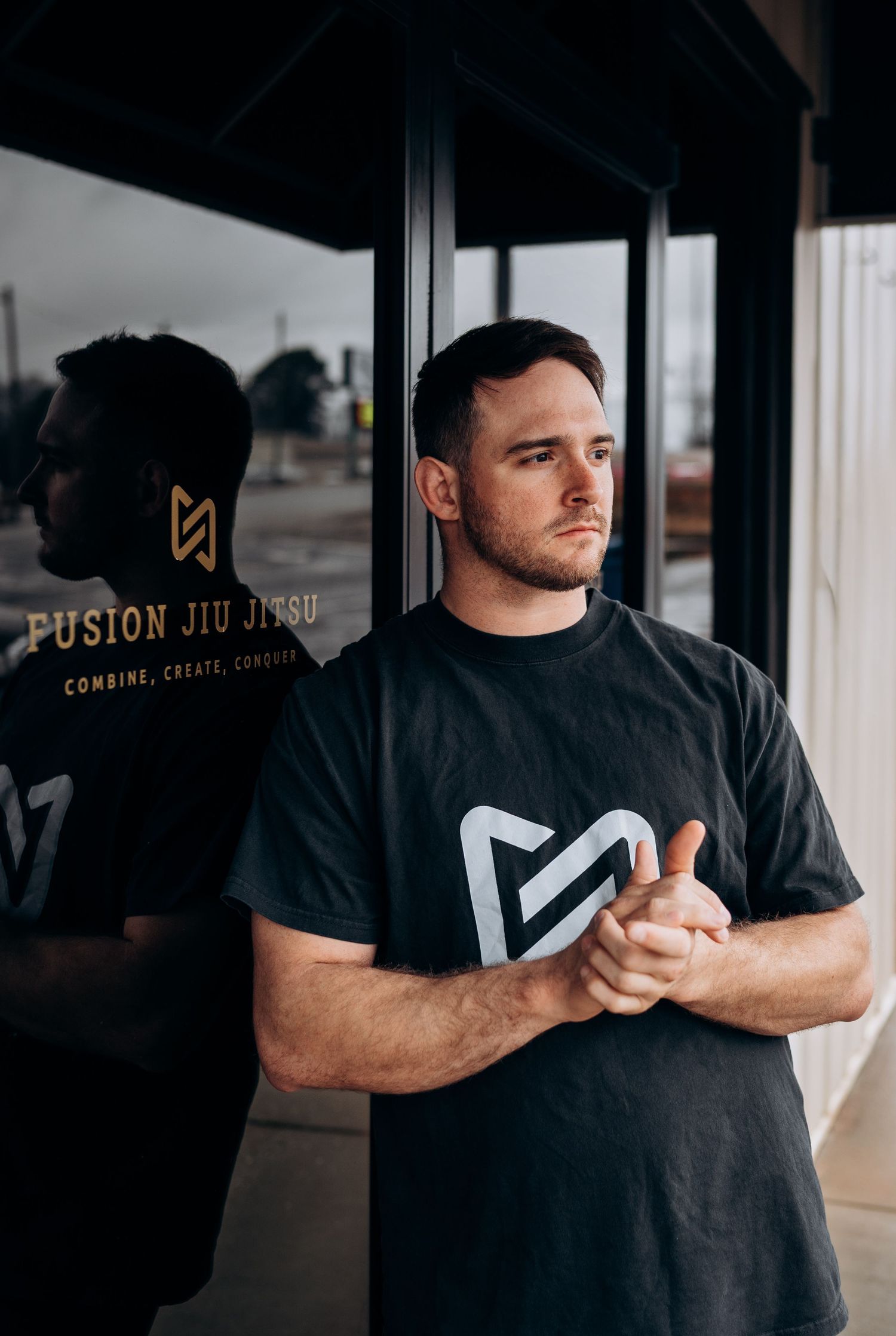 Person in black t-shirt demonstrating martial arts stances in front of Fusion Jiu Jitsu signage.