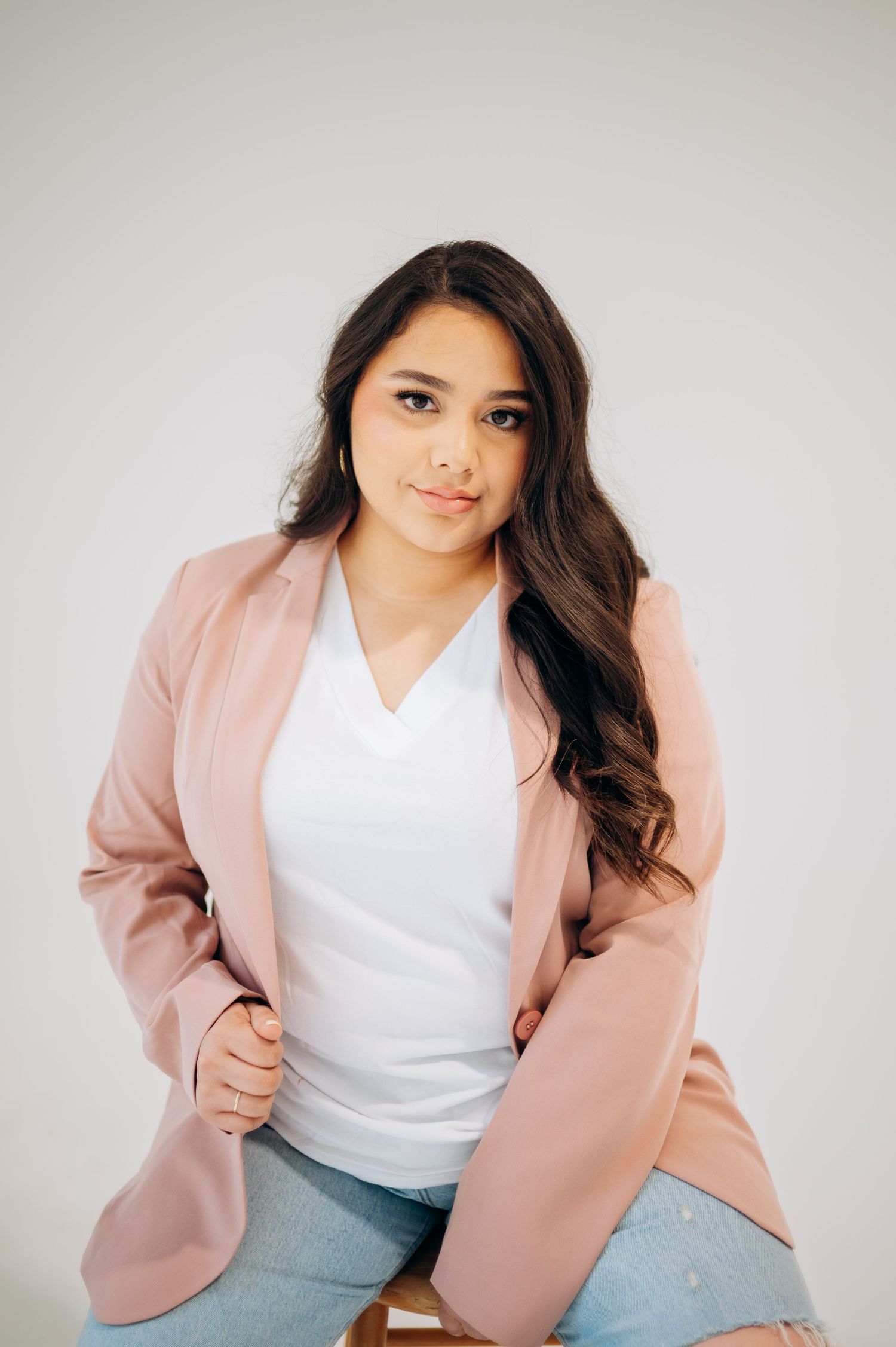 Woman in pink blazer and white top poses confidently in studio setting.