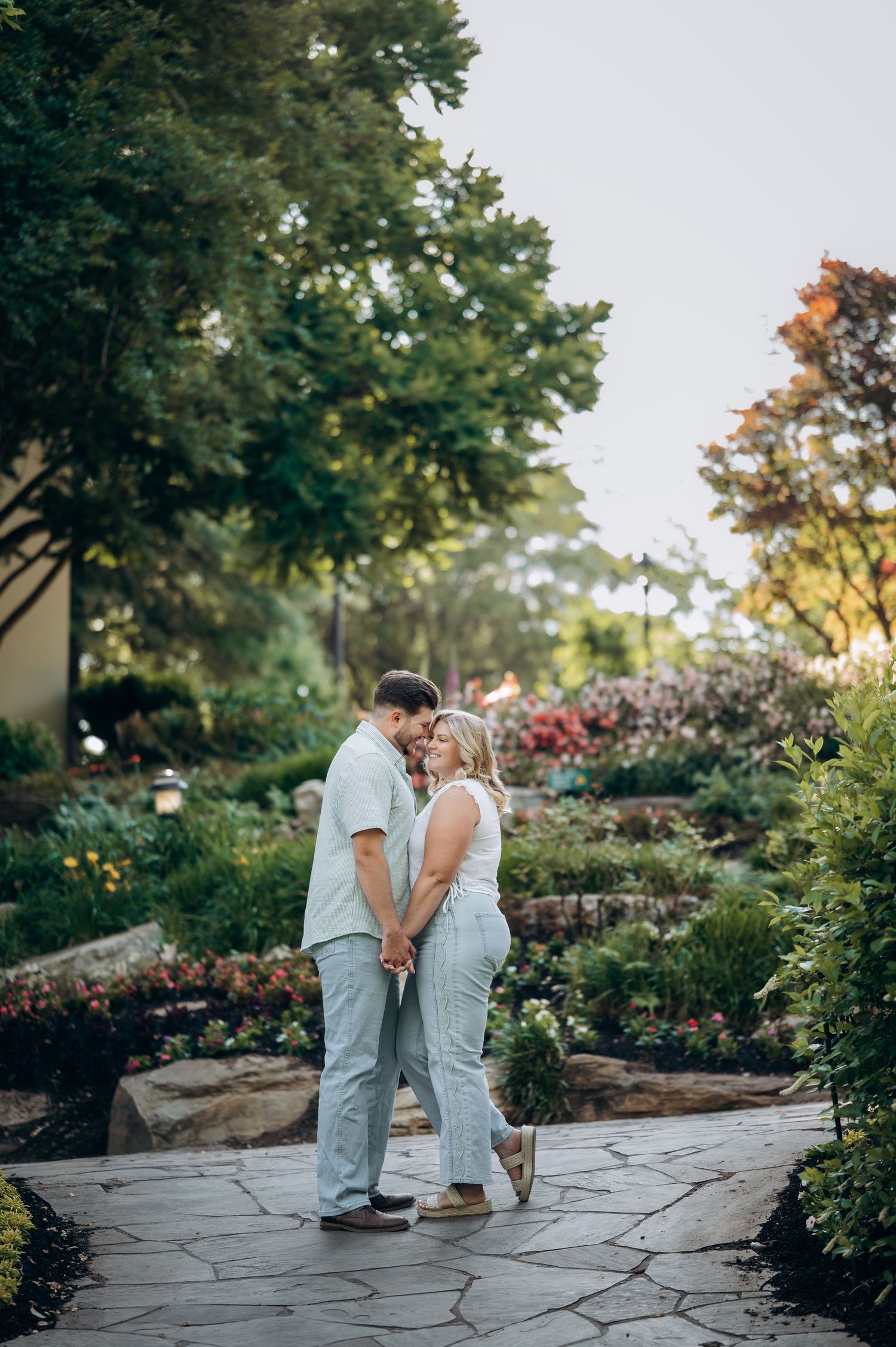 Couple holding hands and sharing a romantic moment on a stone path surrounded by lush garden greenery.