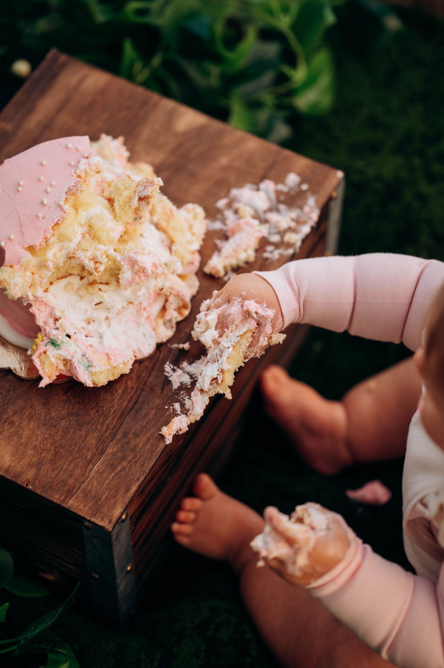 A demolished pink birthday cake sits on a wooden surface with scattered crumbs.
