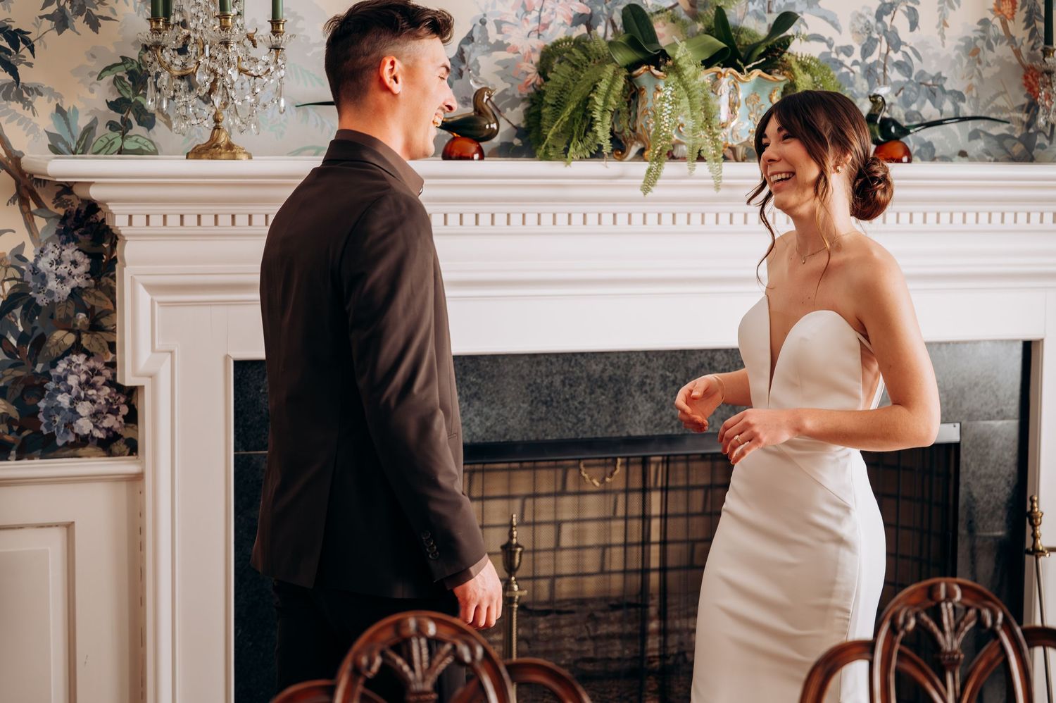Bride and groom sharing first look moment by elegant fireplace in wedding attire.