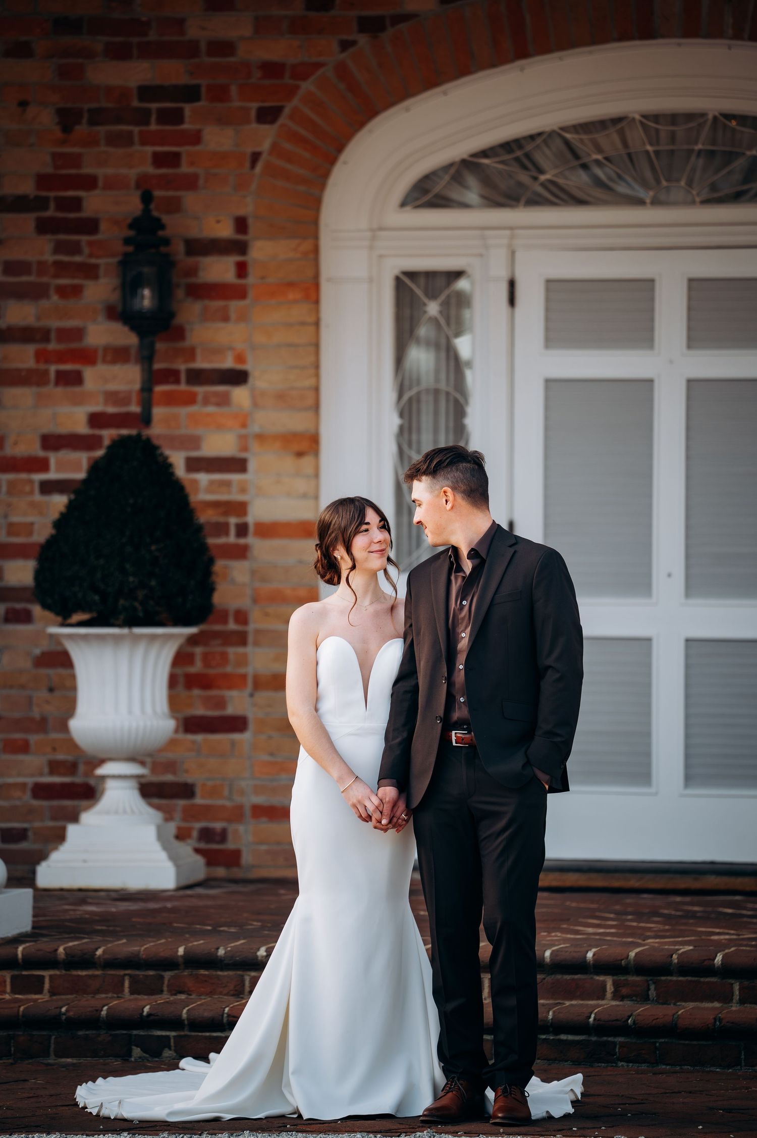Wedding couple poses together on brick porch with white colonial architecture details.