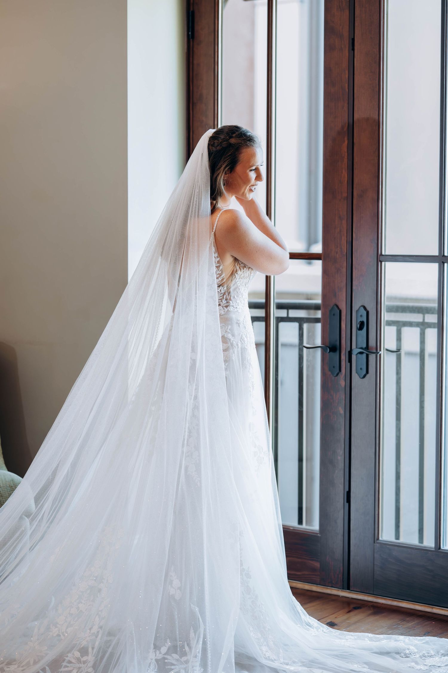 An elegant bridal silhouette in a lace wedding dress with cathedral veil by French doors.