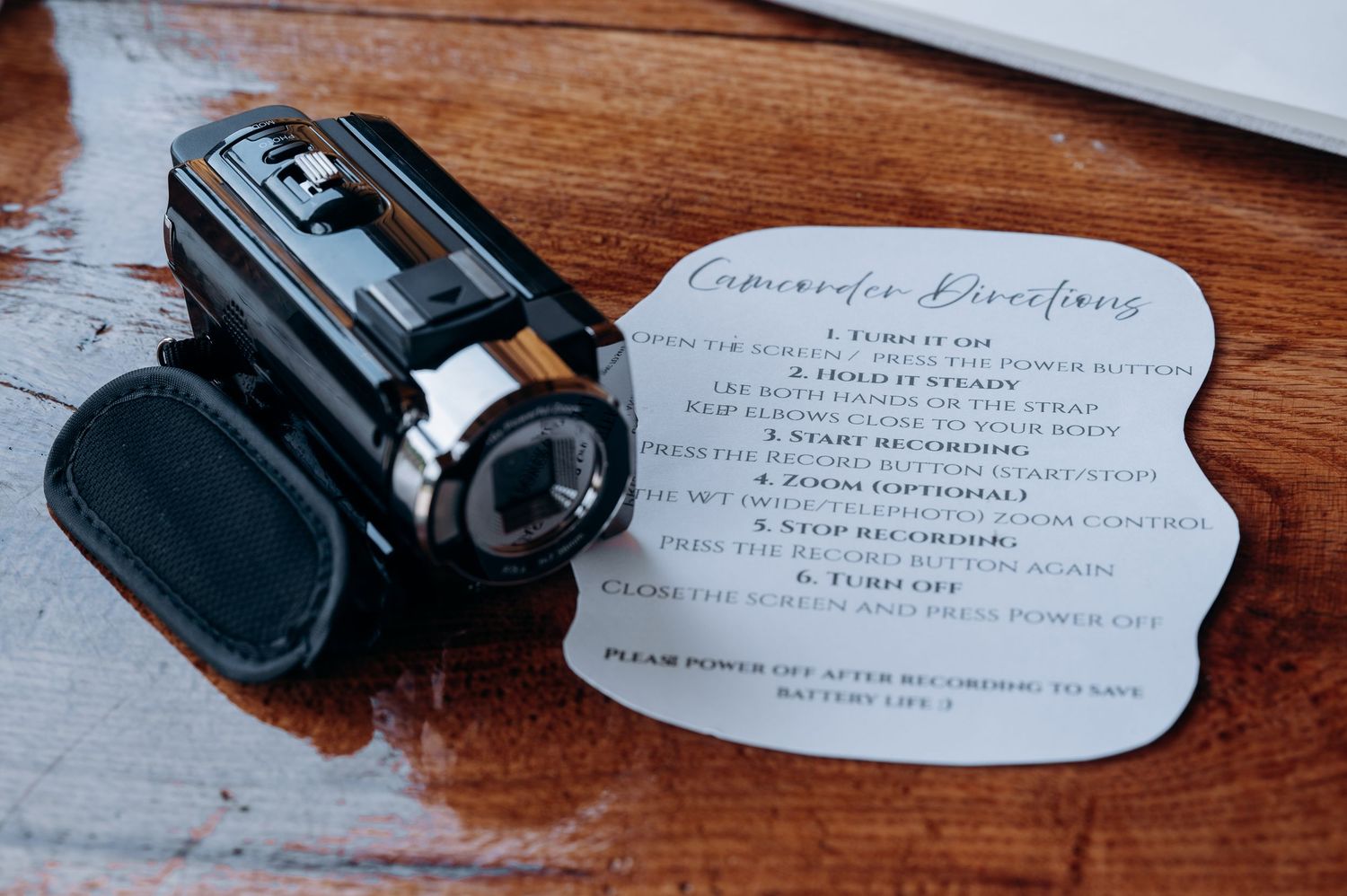 Vintage camcorder with handwritten directions card on wooden table at wedding reception.