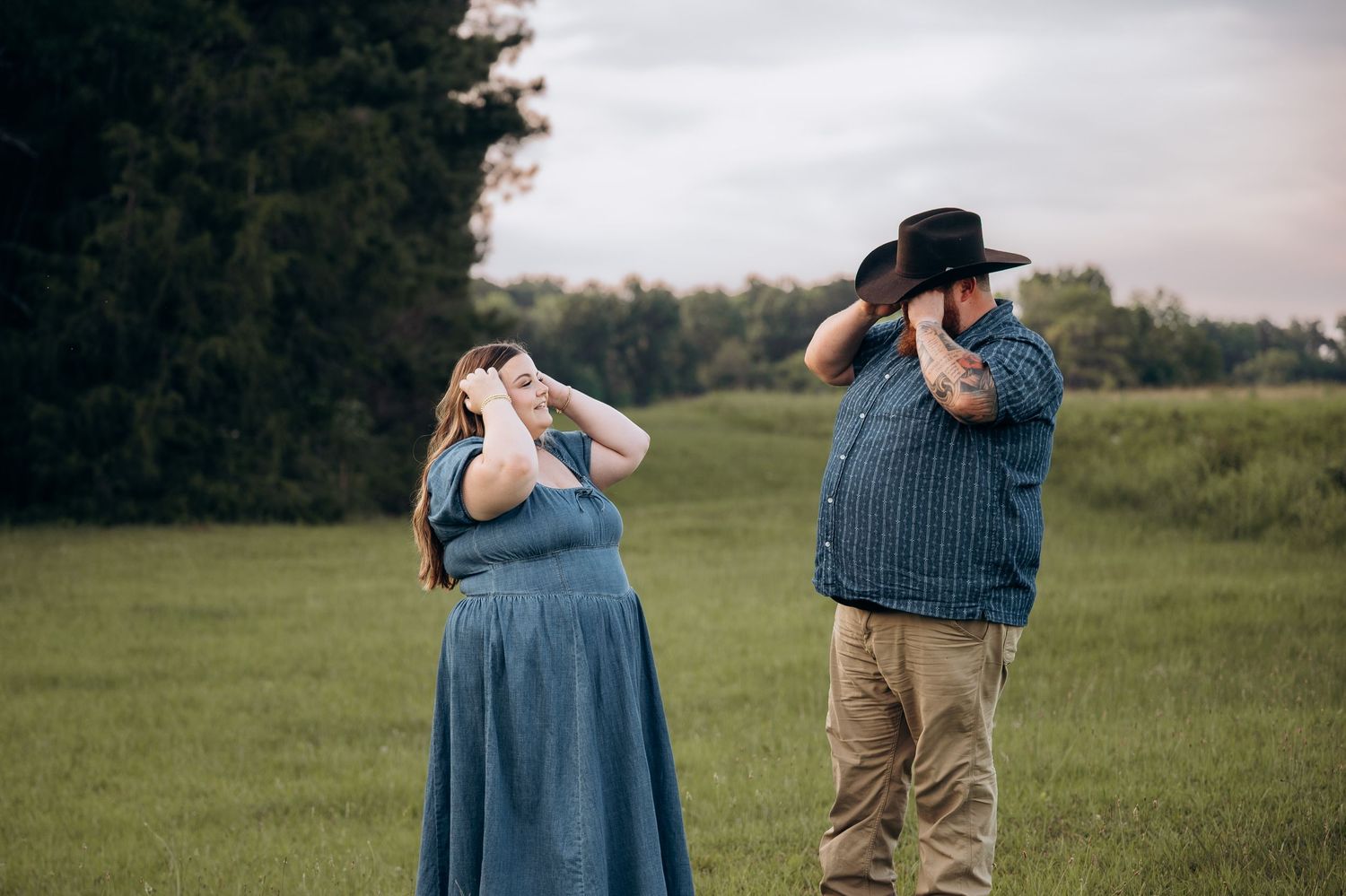 Couple standing in green field both wiping tears, woman in blue dress and man in cowboy hat.