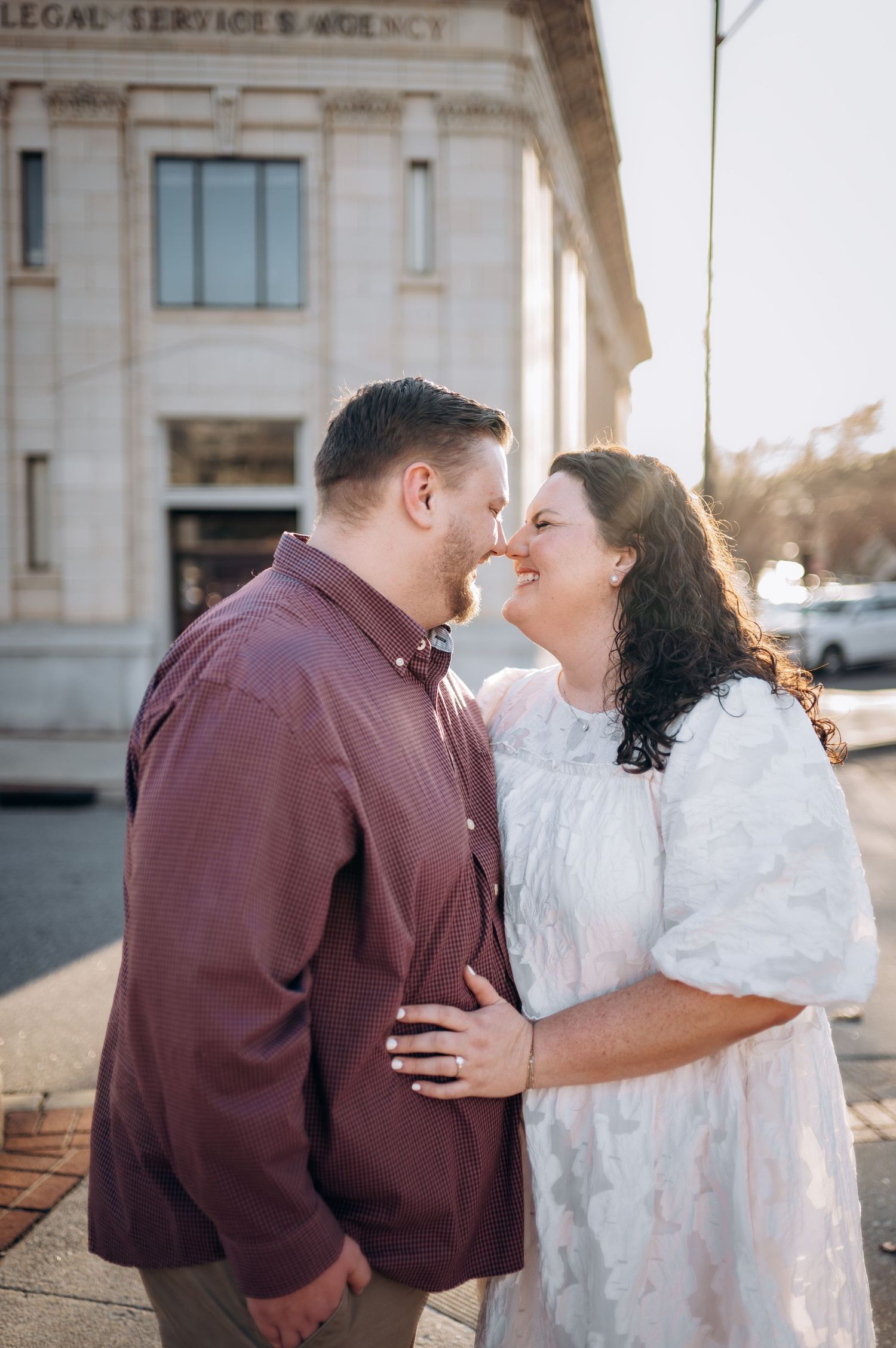 A romantic couple shares an intimate moment outside a historic building during sunset.