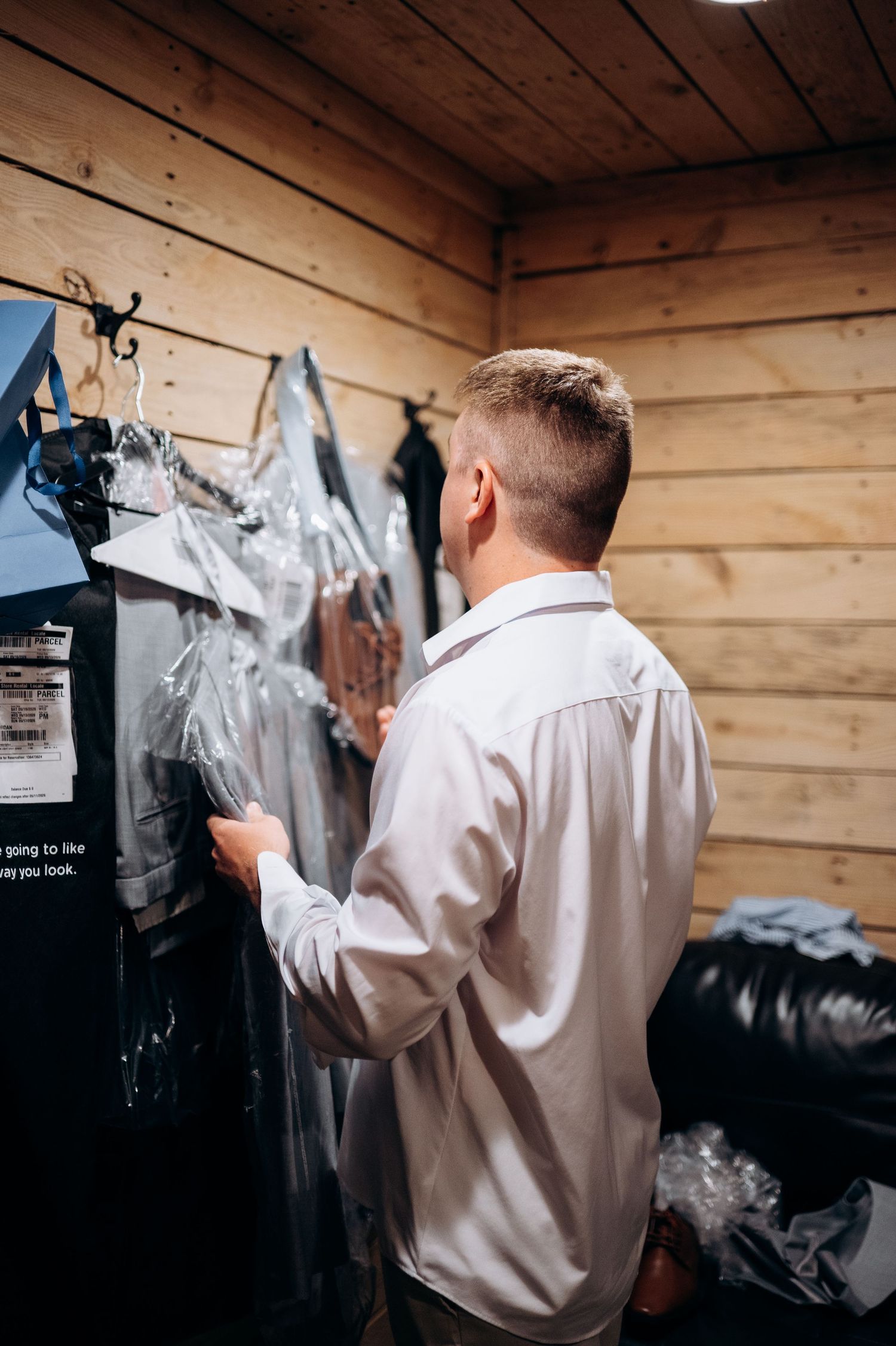 Groom preparing for wedding day, selecting dry-cleaned suit in wooden dressing room.