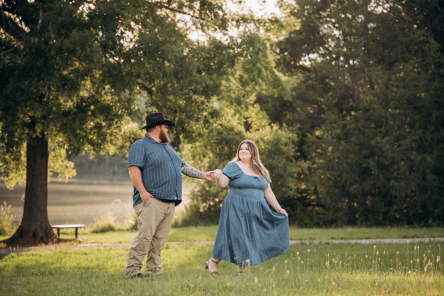 Couple dancing in a sunlit park, woman in blue dress held by man in cowboy hat and plaid shirt.