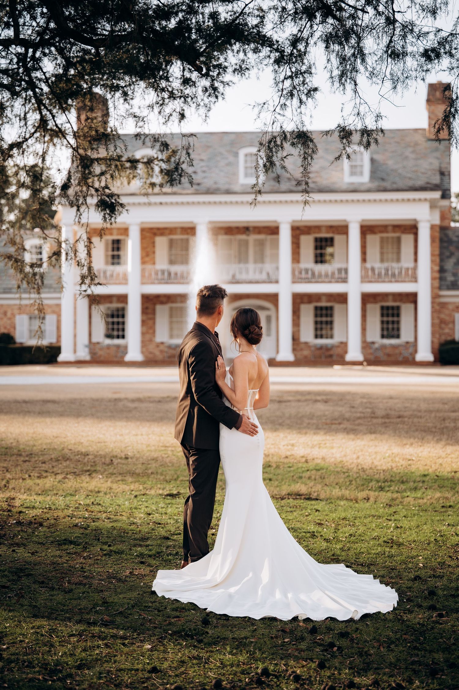Elegant wedding couple standing on lawn before grand southern plantation house with white columns.