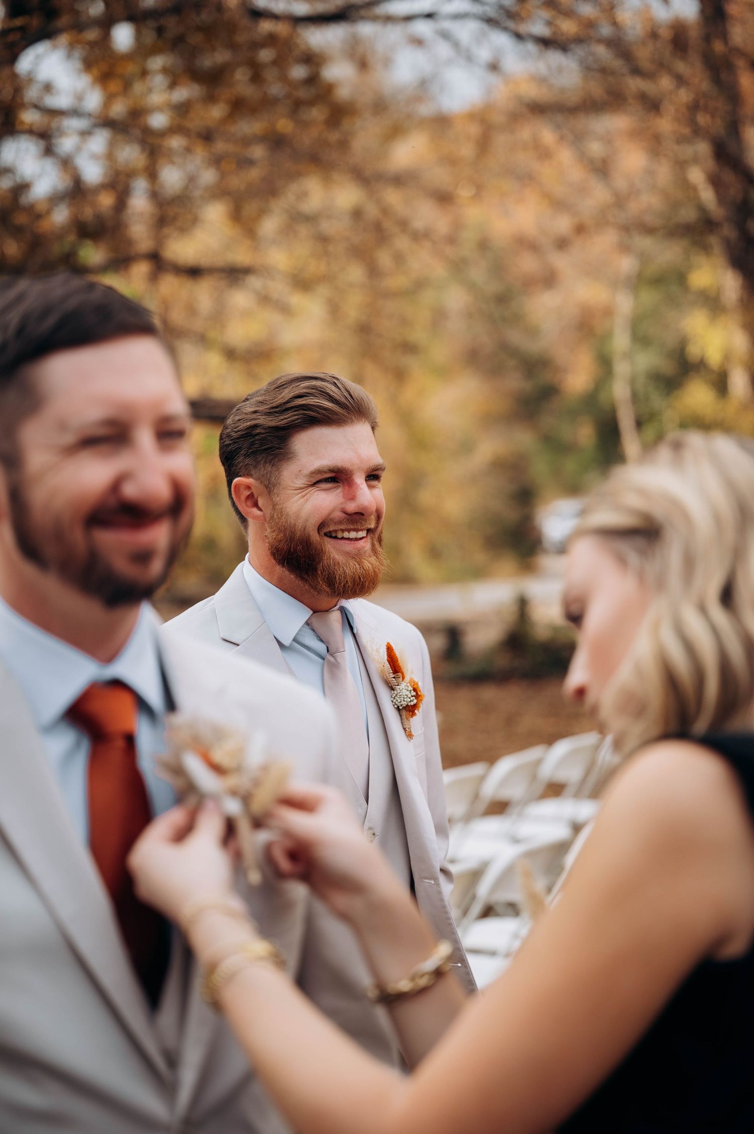 Groomsmen in light gray suits share laughs during outdoor fall wedding.
