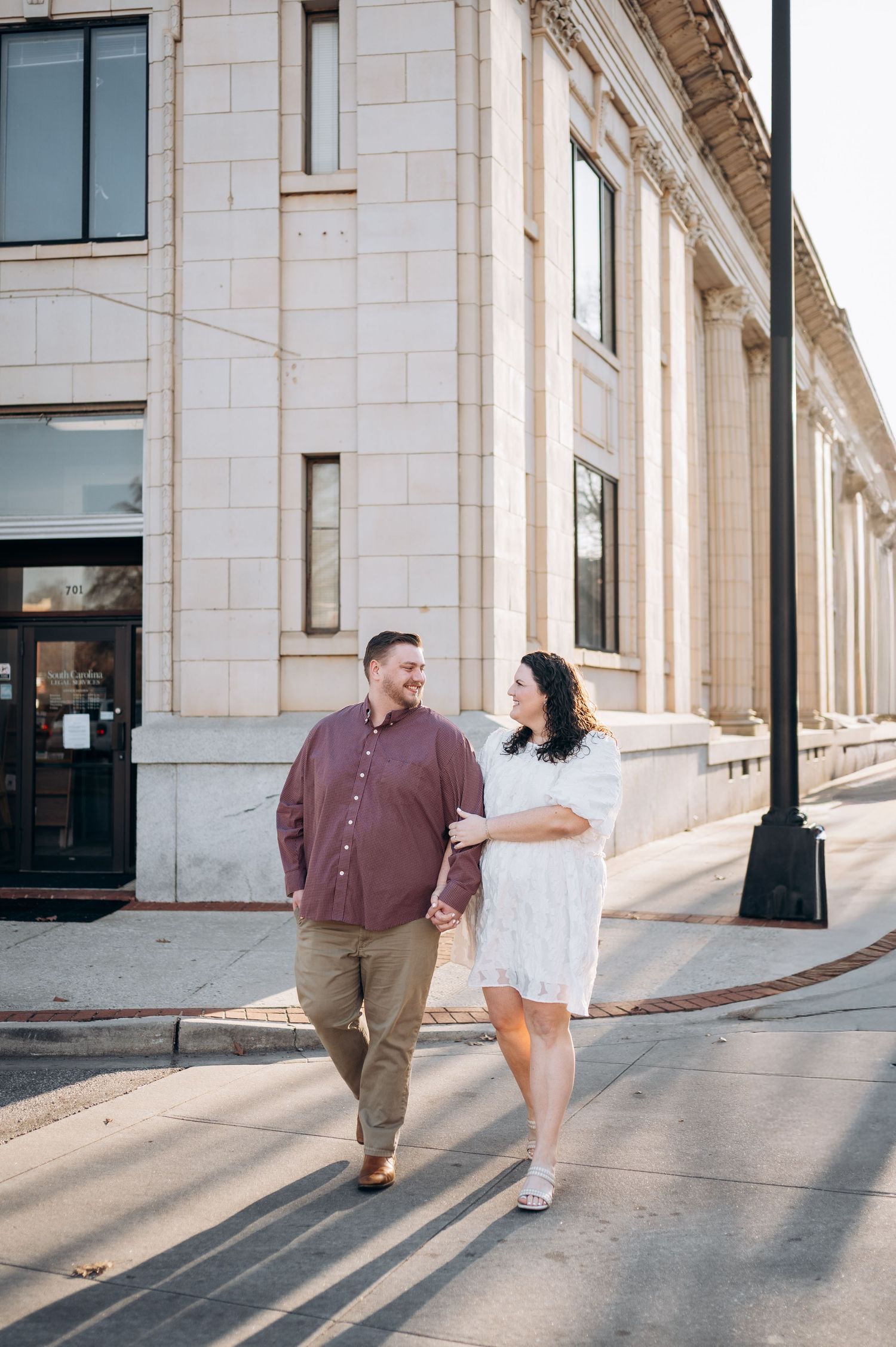 A couple shares playful moments while walking along a columned building exterior in a romantic photoshoot sequence.