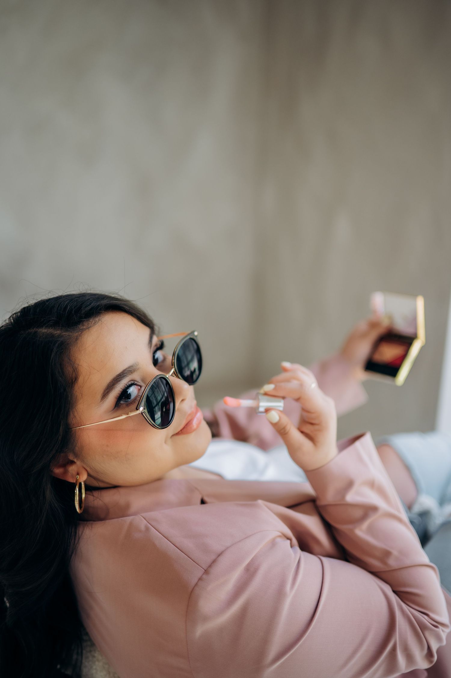 Person in pink blazer relaxes on white furniture while wearing dark sunglasses.