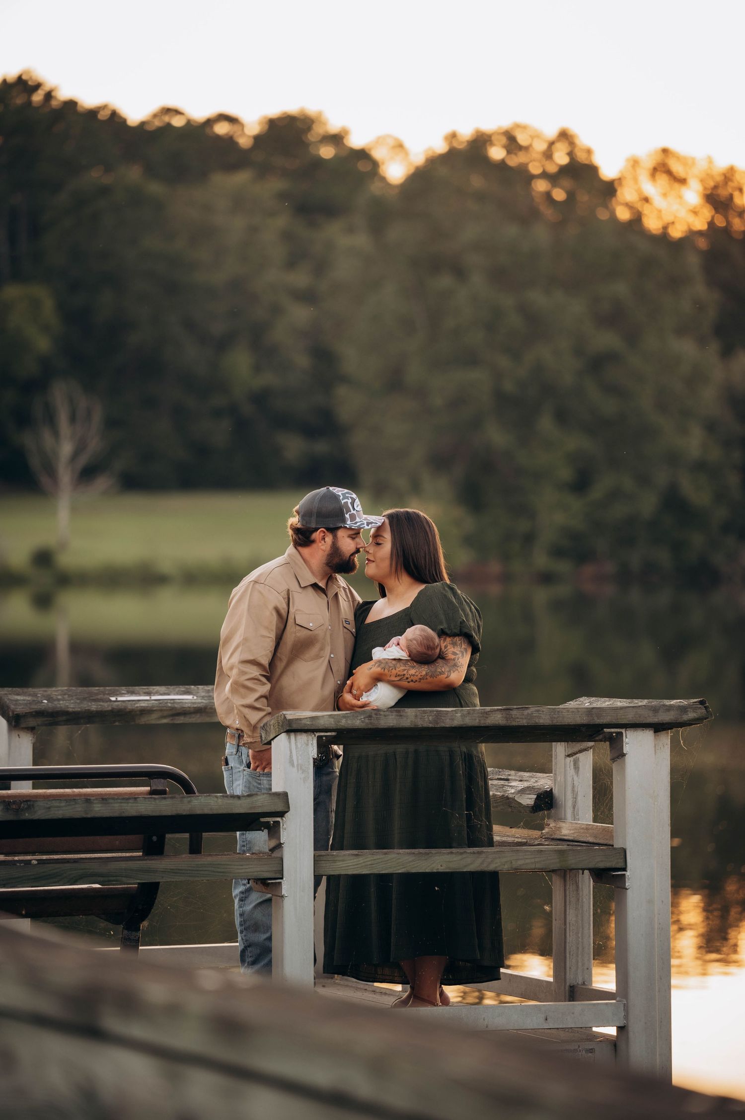 Parents admiring their newborn baby while sitting on rustic wooden dock.
