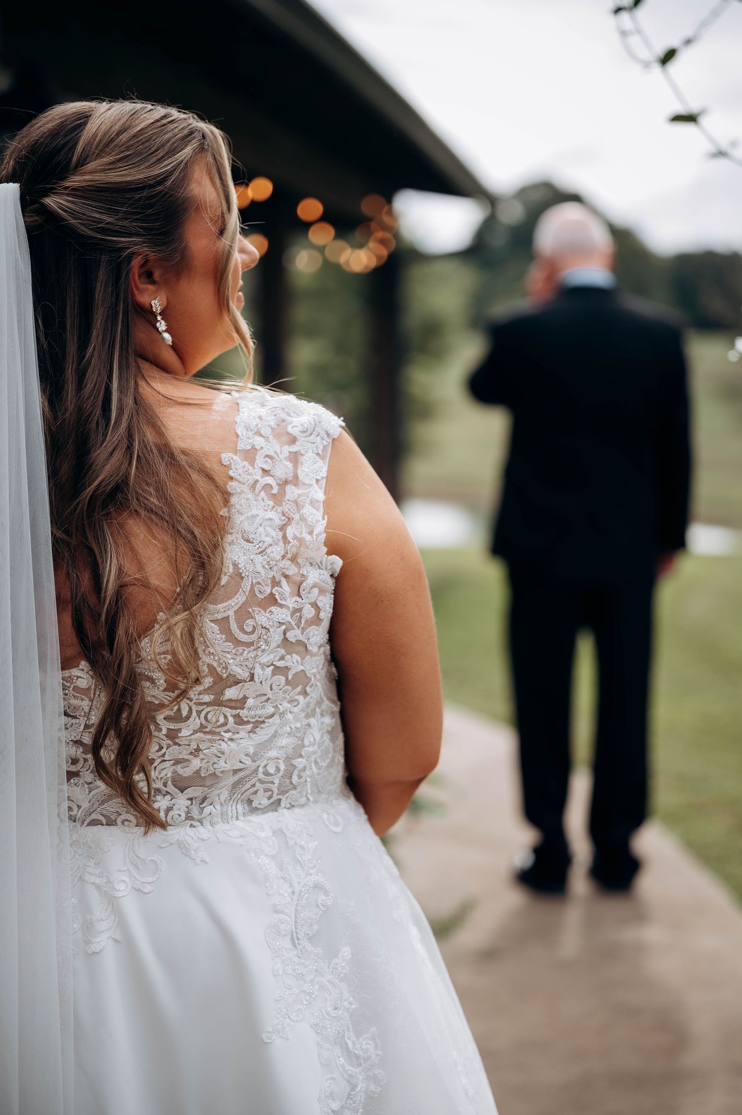 Back view of bride in lace wedding dress with veil standing on covered walkway.